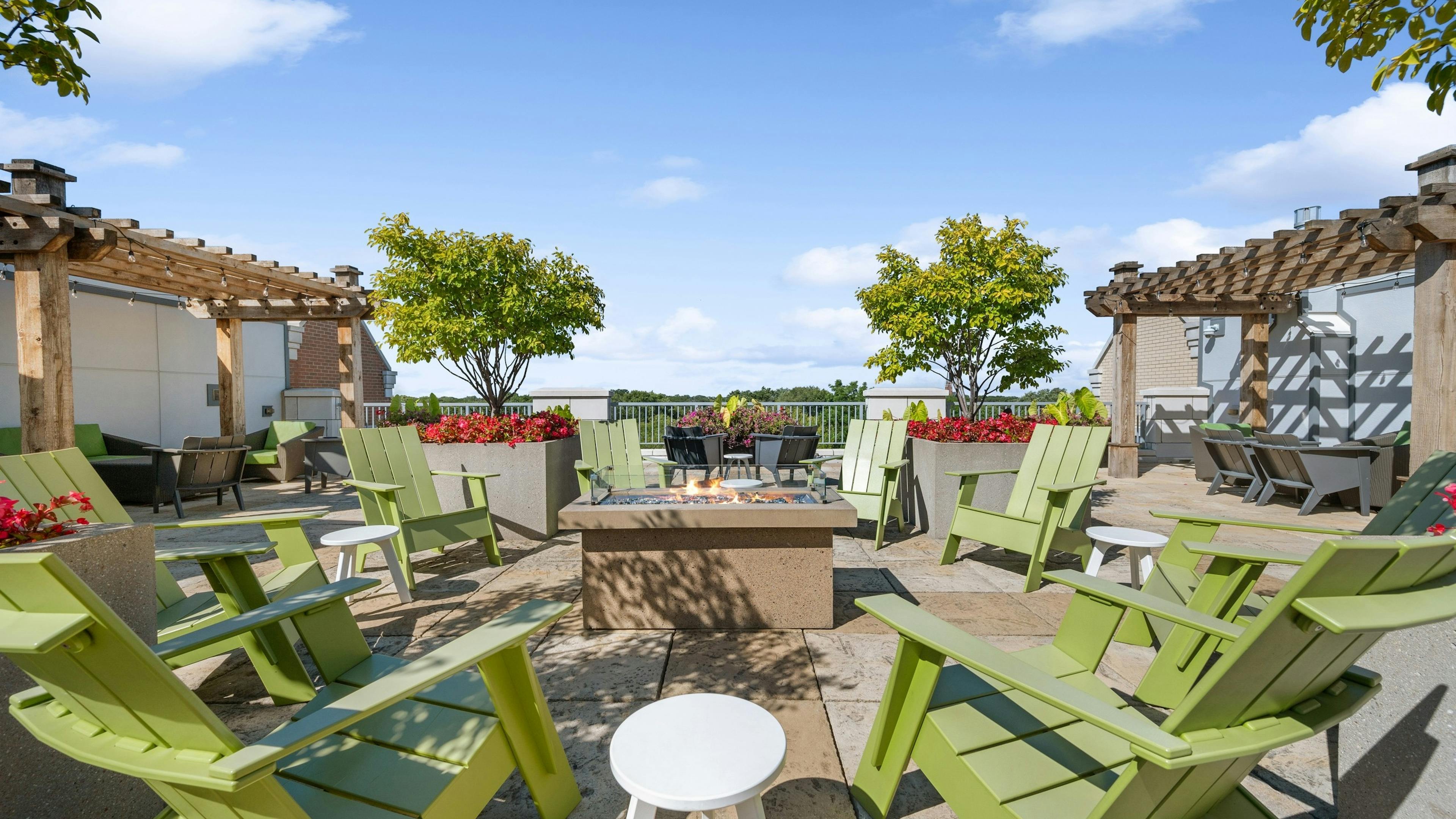 AMLI Evanston rooftop with green Adirondack chairs surrounding lit firepit with pergolas and potted trees and flowers