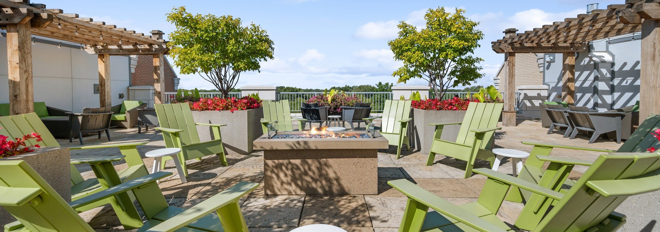 AMLI Evanston rooftop with green Adirondack chairs surrounding lit firepit with pergolas and potted trees and flowers