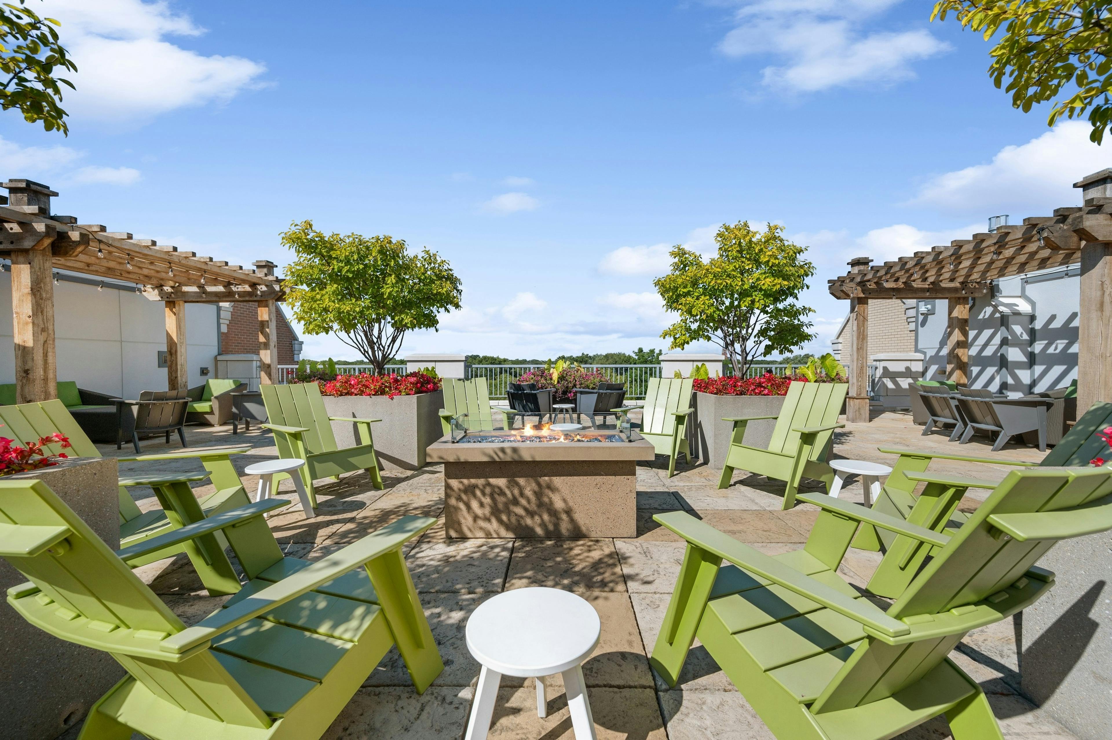AMLI Evanston rooftop with green Adirondack chairs surrounding lit firepit with pergolas and potted trees and flowers