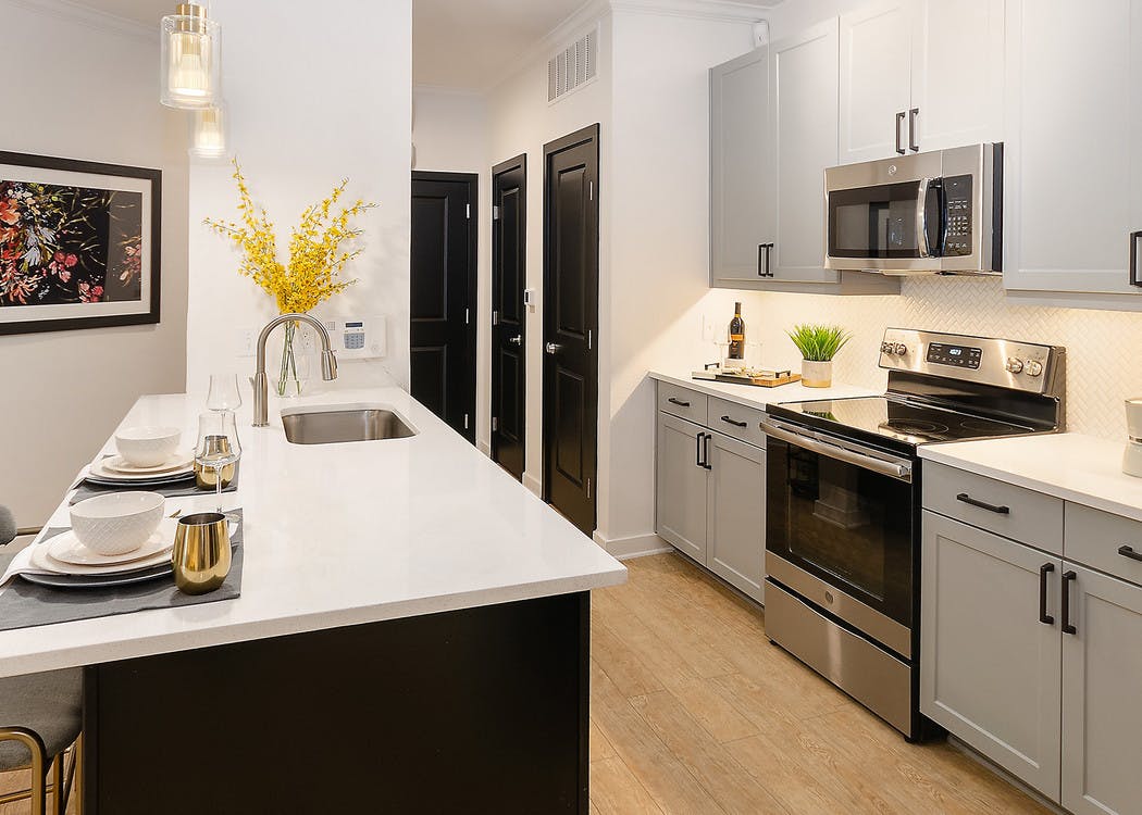 Kitchen at AMLI Quadrangle with white cabinets and countertops with stainless steel appliances and light wood flooring