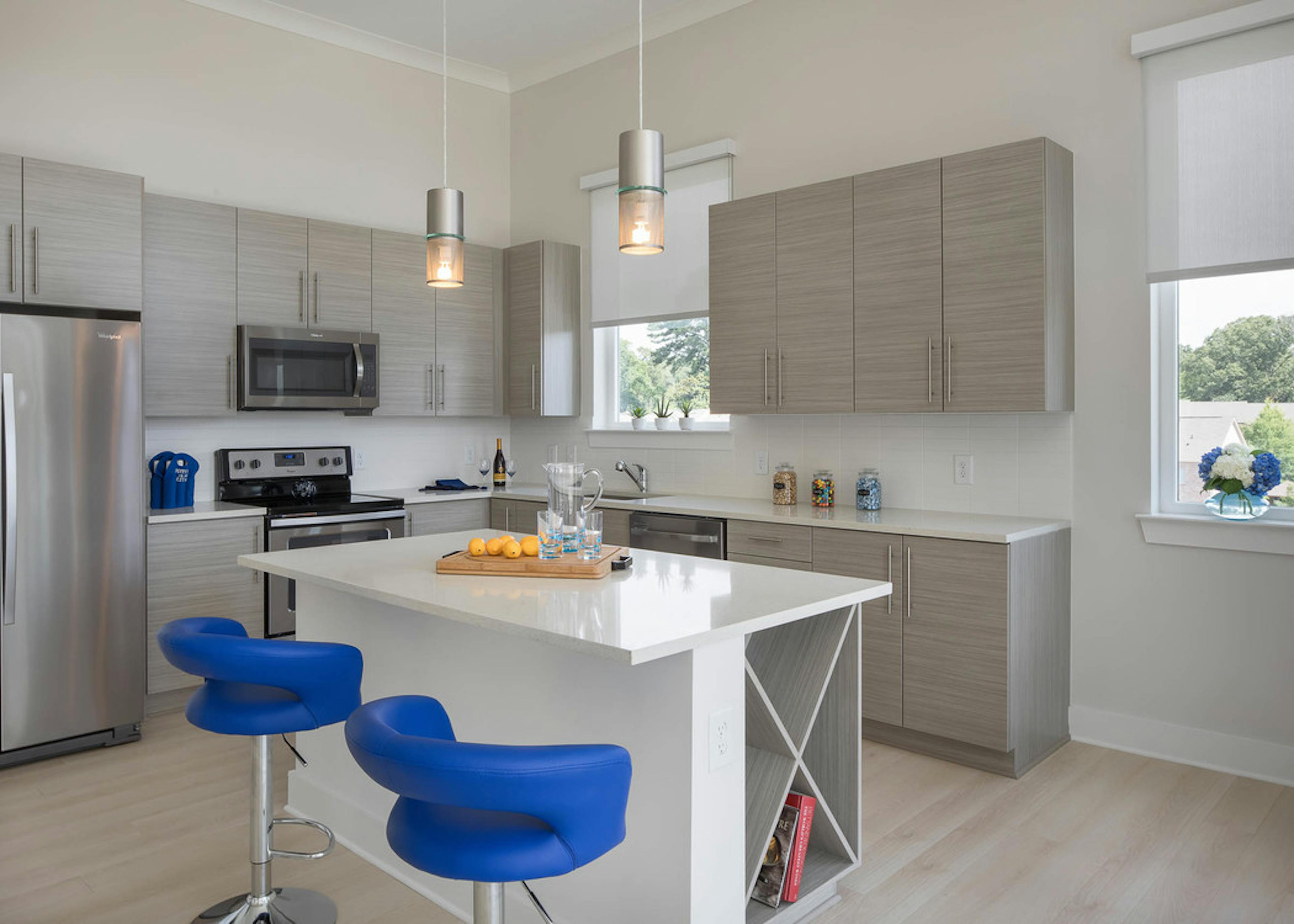 Interior of AMLI Buckhead kitchen with grey cabinets and sleek white countertops with stainless steel appliances and island