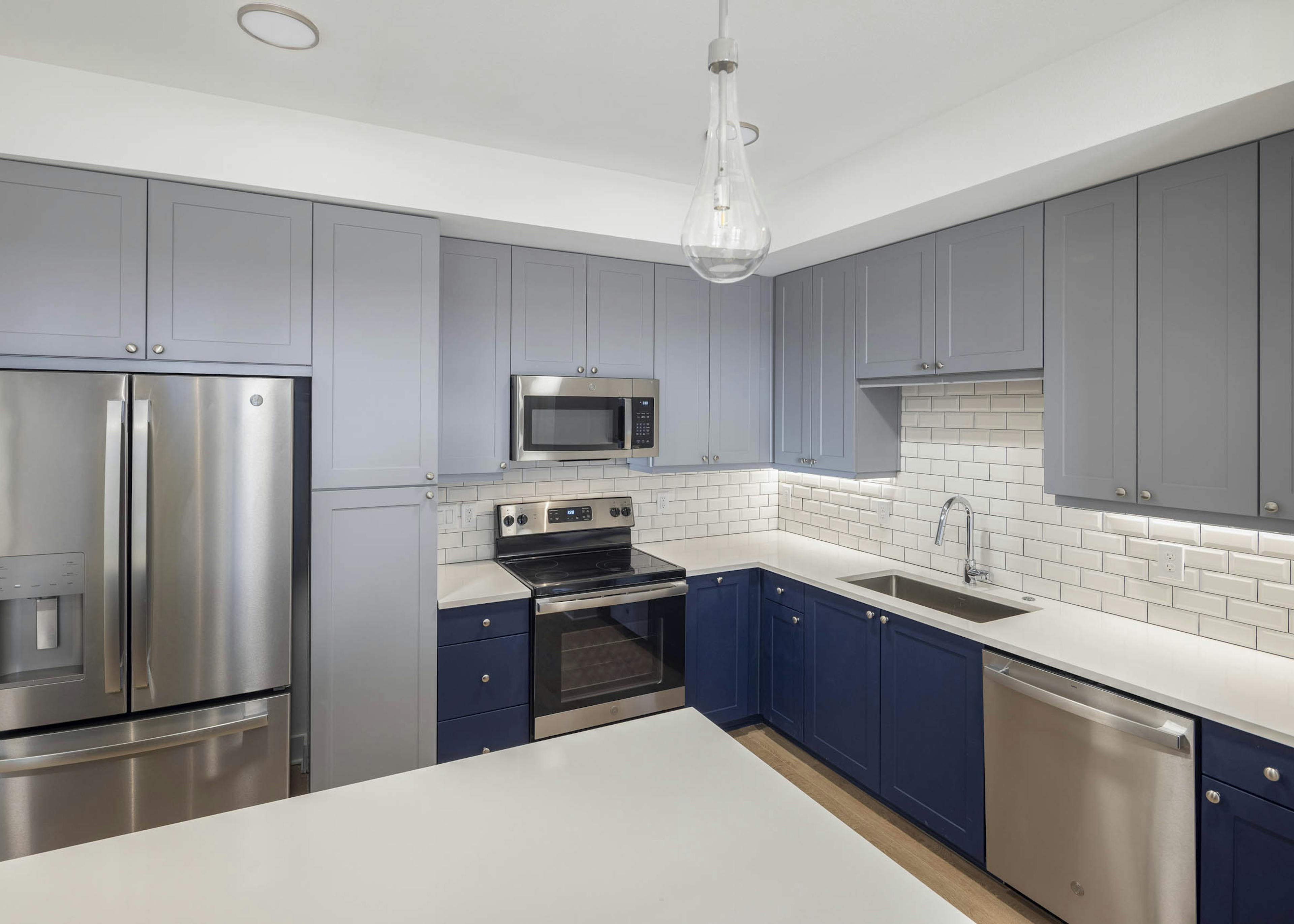 AMLI Branch Park apartment kitchen with blue cabinets and white subway tiled backsplash featuring stainless steel appliances