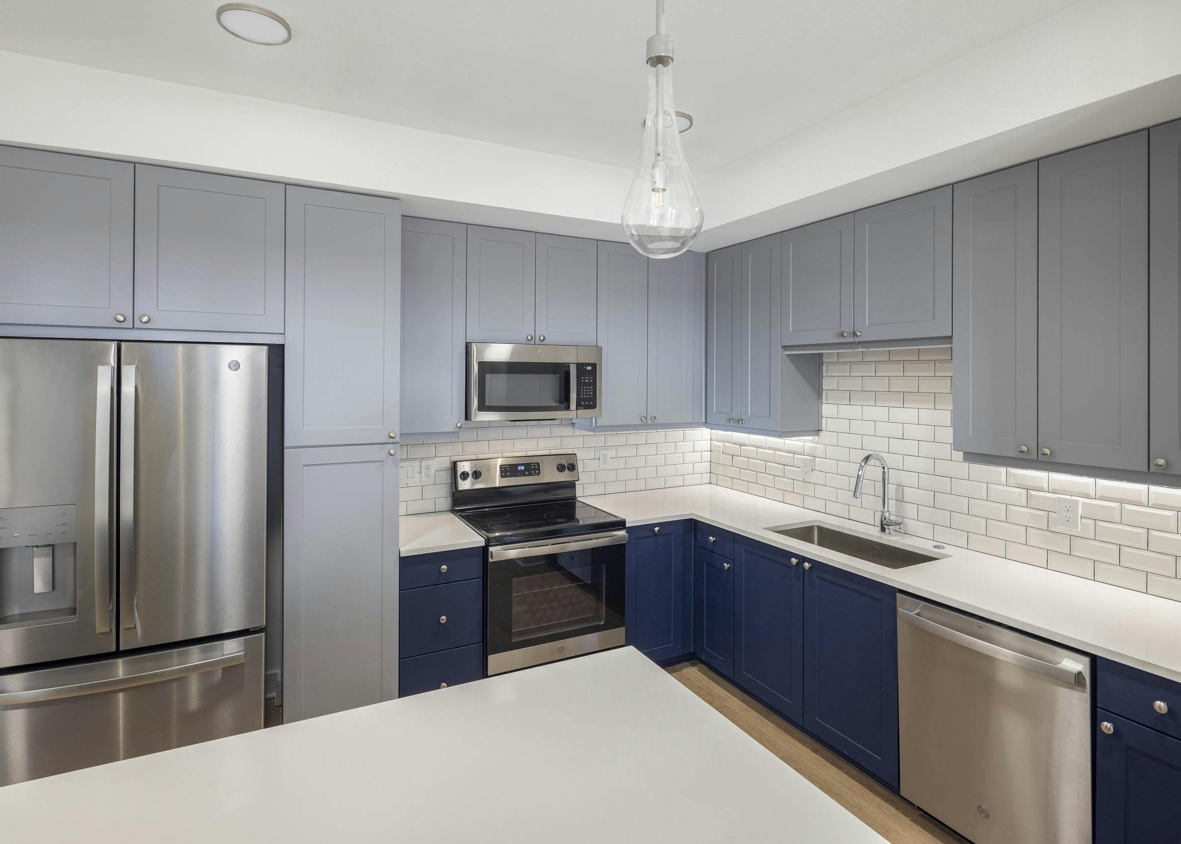 AMLI Branch Park apartment kitchen with blue cabinets and white subway tiled backsplash featuring stainless steel appliances