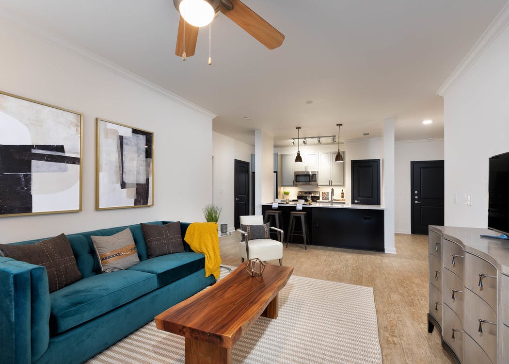 View of living room and kitchen at AMLI Quadrangle with light hardwood floors and neutral walls with blue velvet couch