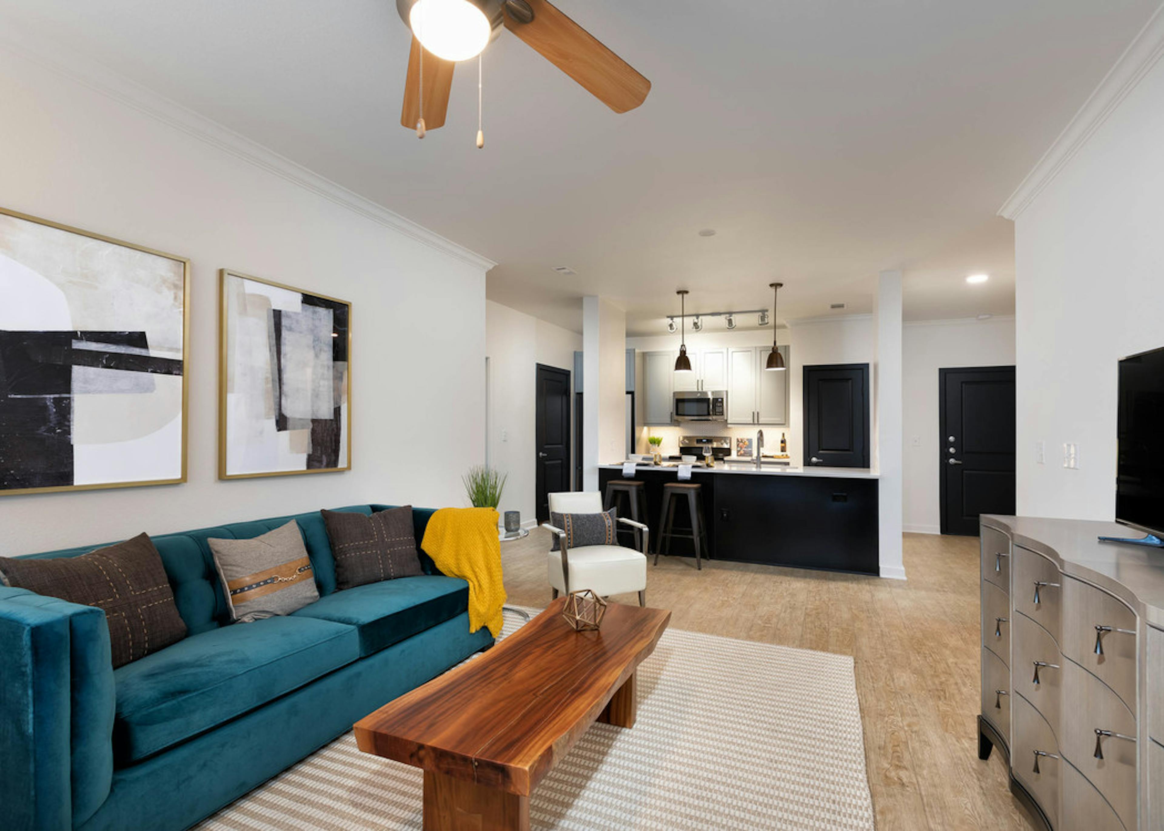 View of living room and kitchen at AMLI Quadrangle with light hardwood floors and neutral walls with blue velvet couch