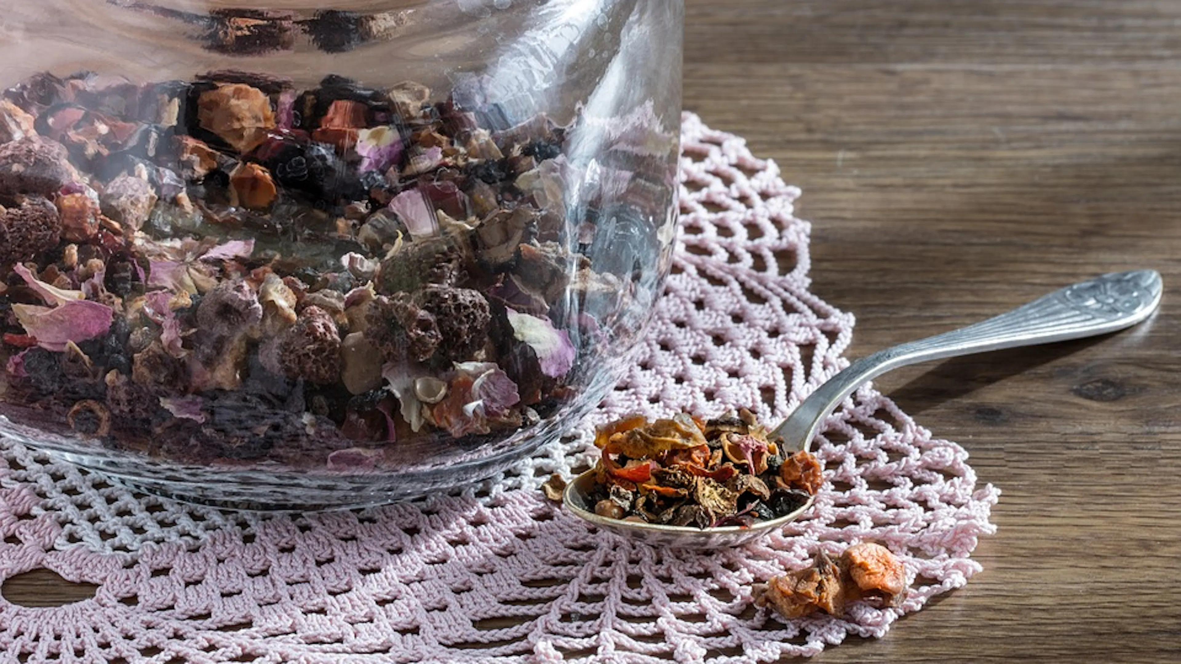 A close up of a glass jar filled with herbal tea and a spoon resting beside the jar with tea in it
