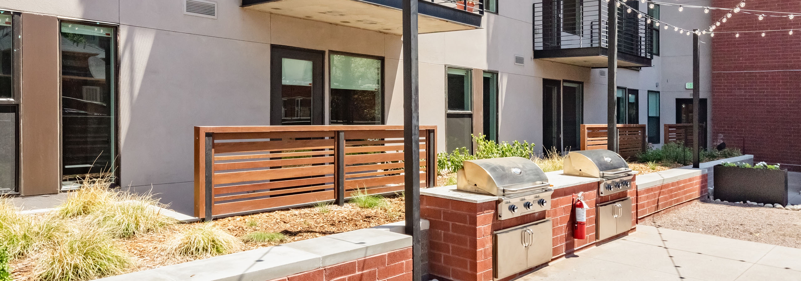 Outdoor grilling area at AMLI at Uptown surrounded by red brick and beige building facade with overhead string lights