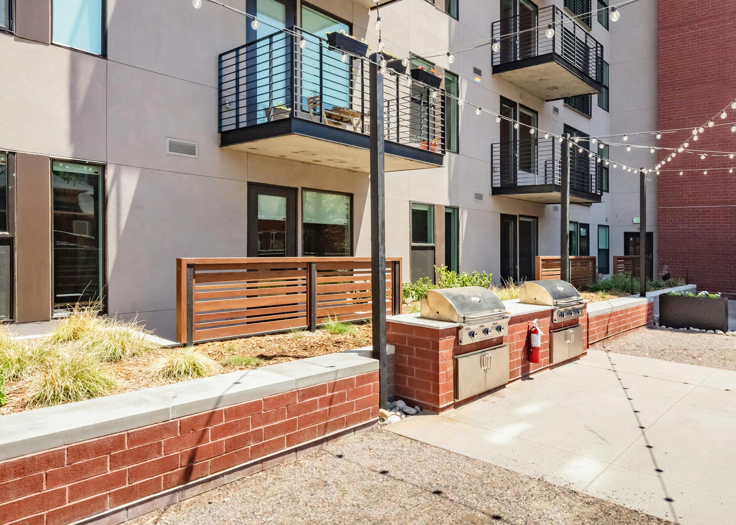 Outdoor grilling area at AMLI at Uptown surrounded by red brick and beige building facade with overhead string lights