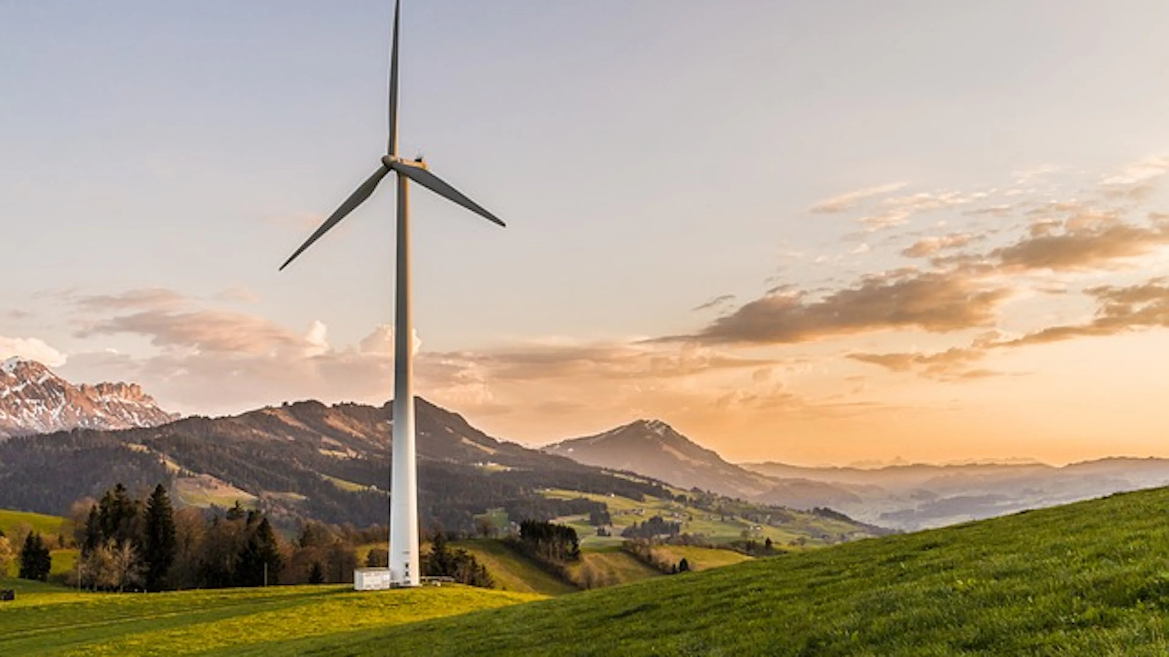 A wind turbine in a meadow with mountains in the background