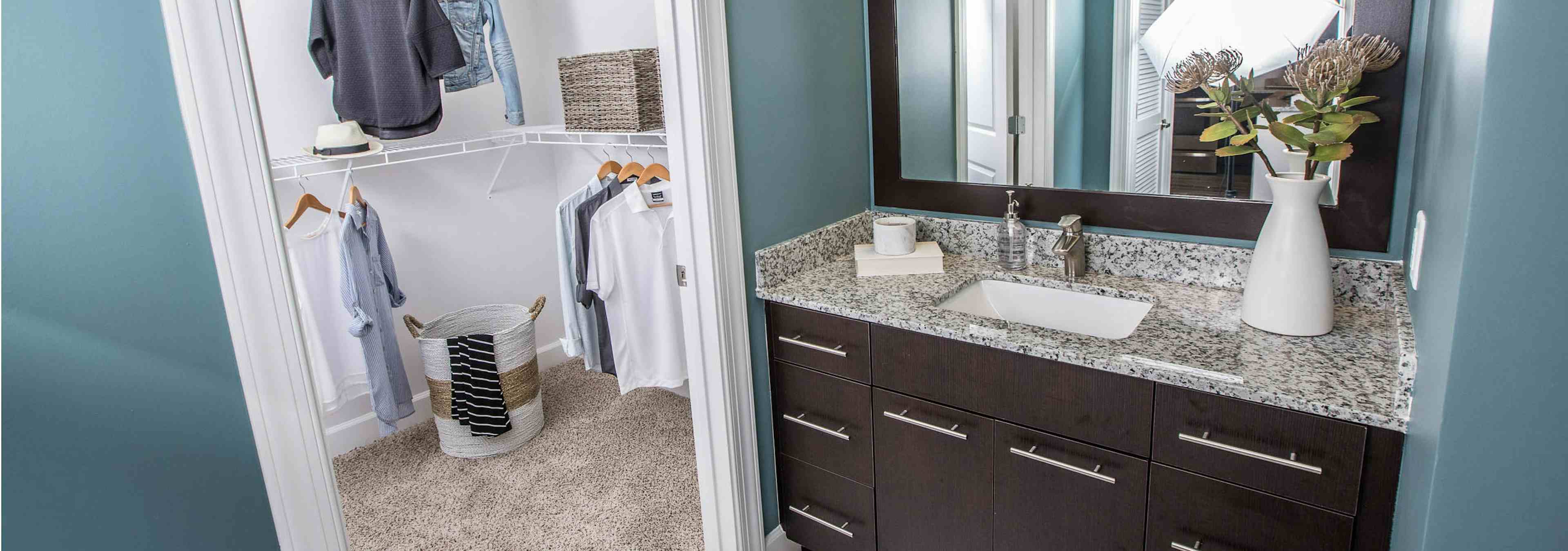 Interior view of AMLI Joya apartment bathroom with single sink vanity, granite counters, mirror, and walk-in closet