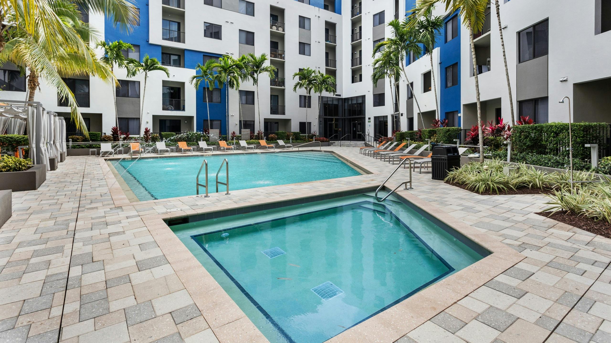 The pool at AMLI 8800 with water feature over pool and adjacent spa with gray and orange lounge chairs and cabanas