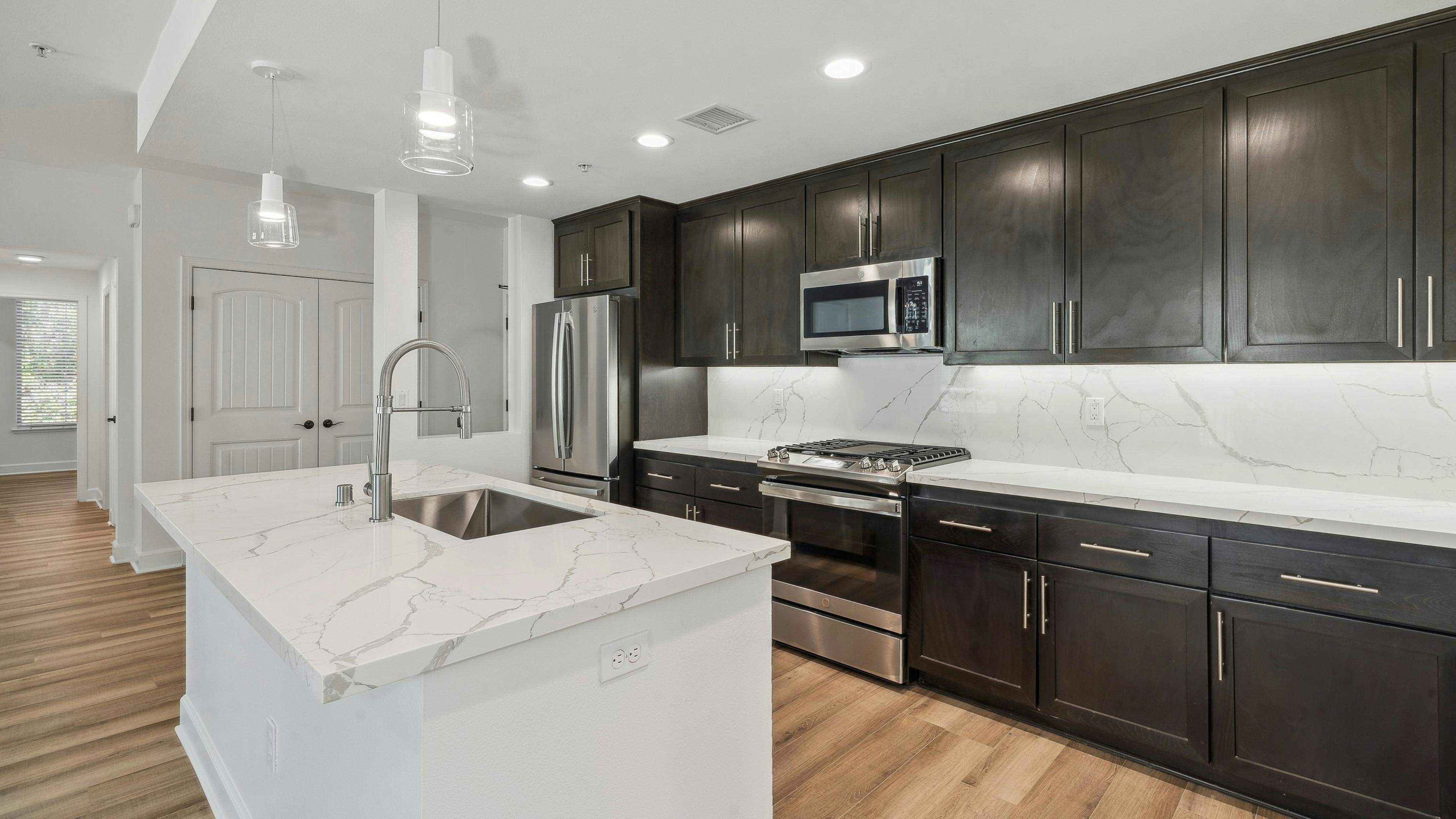 Interior view of island kitchen with dark brown cabinetry and white quartz countertops at AMLI Spanish Hills 