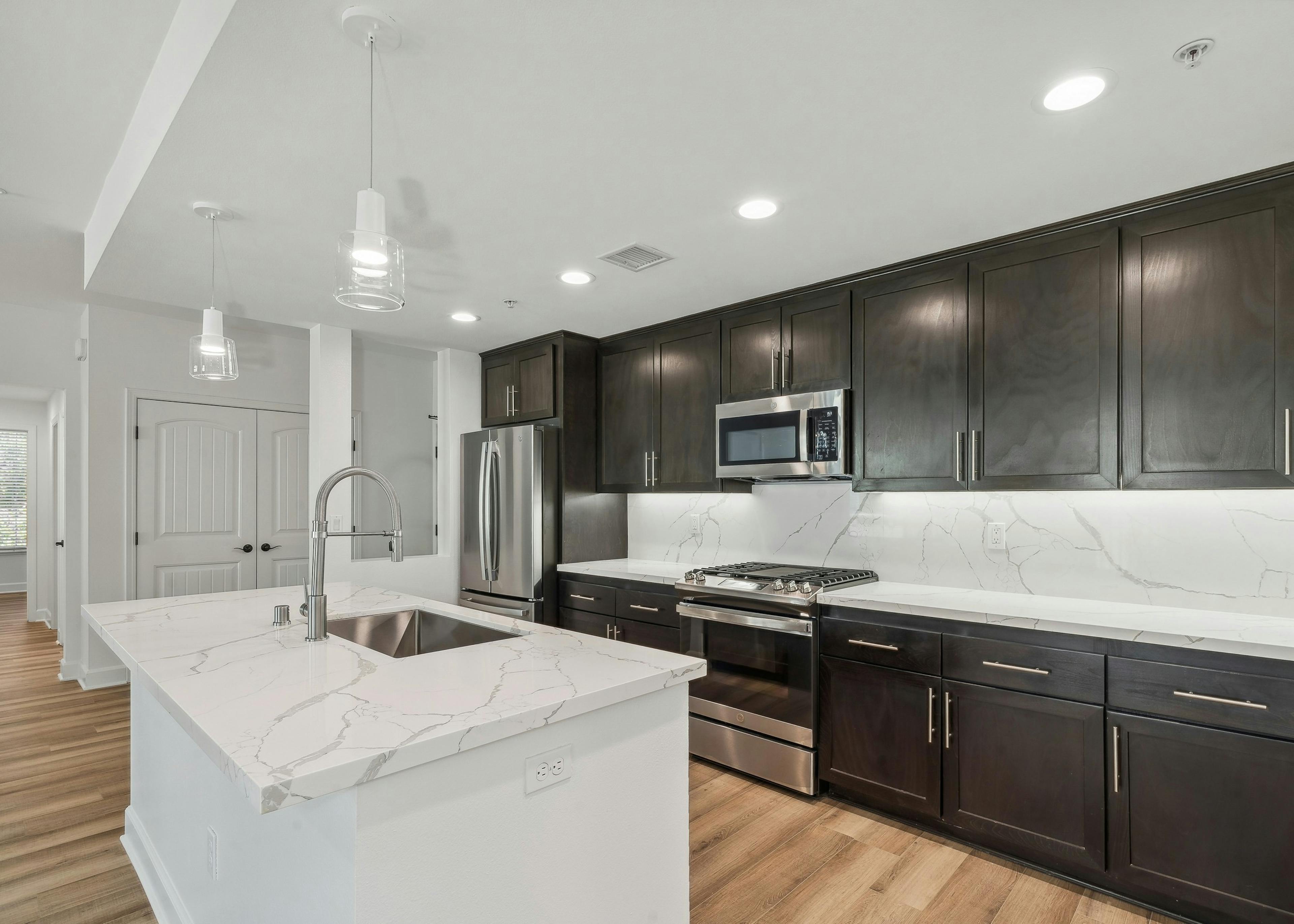 Interior view of island kitchen with dark brown cabinetry and white quartz countertops at AMLI Spanish Hills 