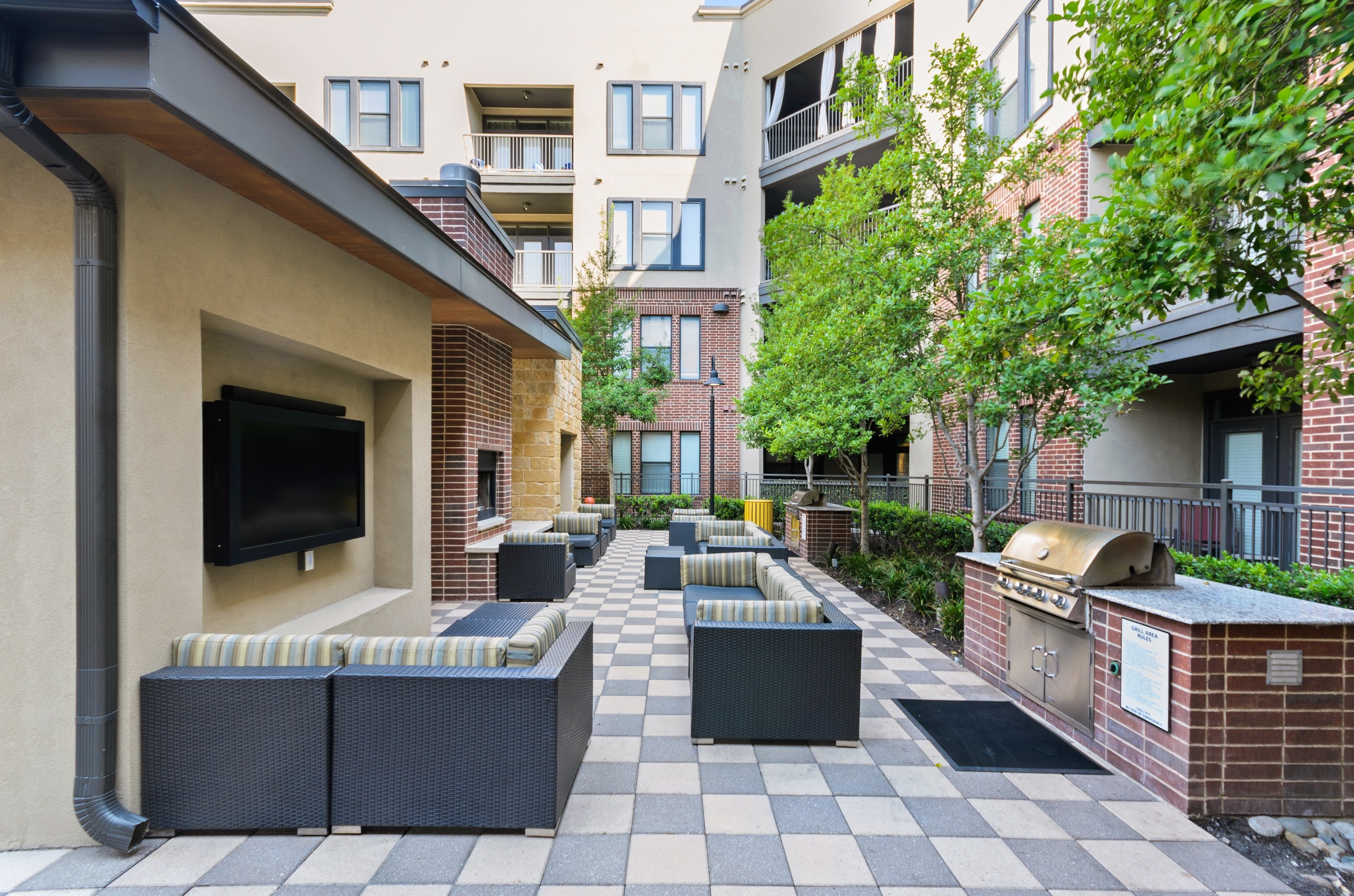 Resident grill station at AMLI West Plano featuring two stainless grills and lounge seating with striped cushions facing wall TVs