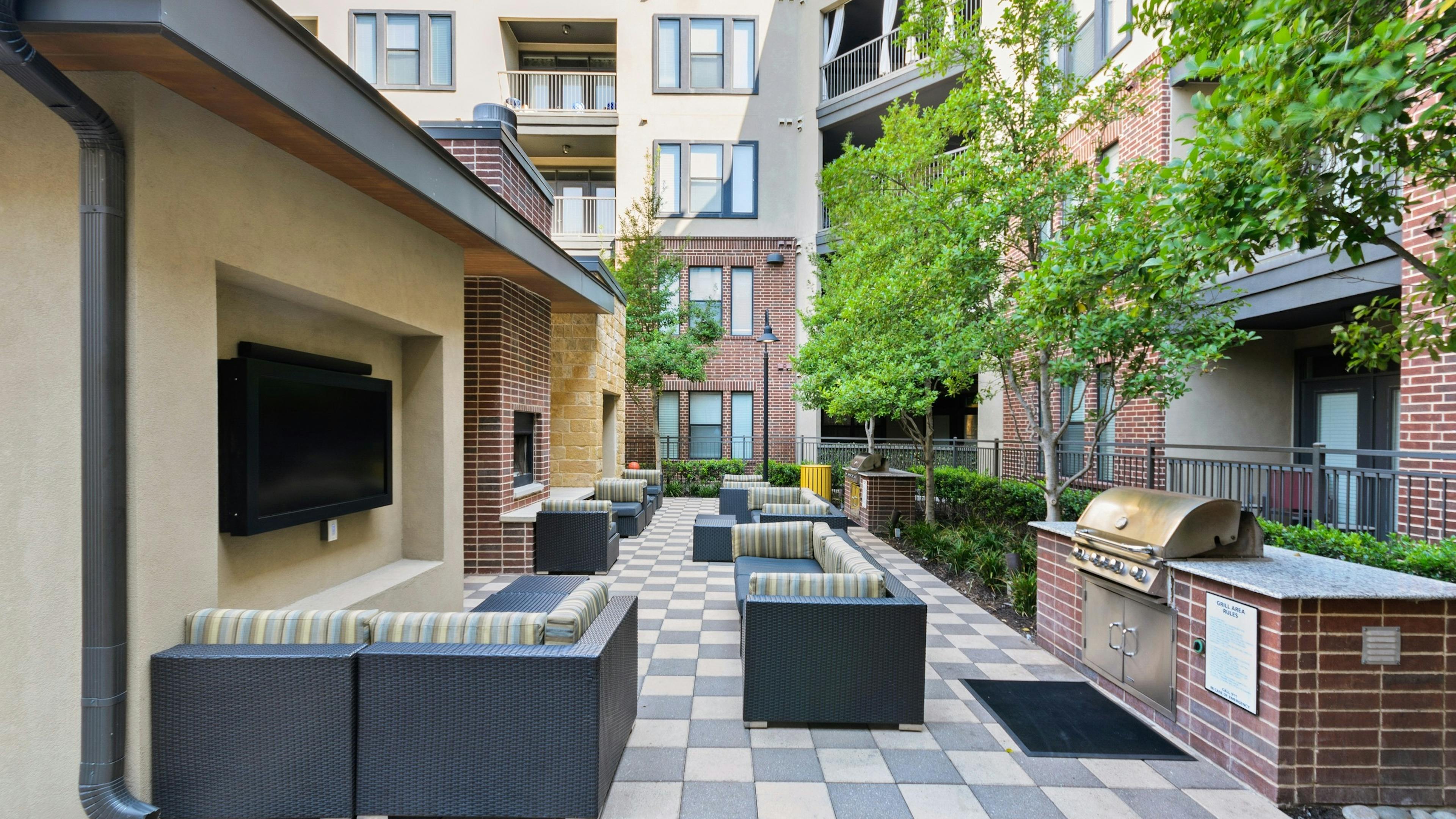 Resident grill station at AMLI West Plano featuring two stainless grills and lounge seating with striped cushions facing wall TVs