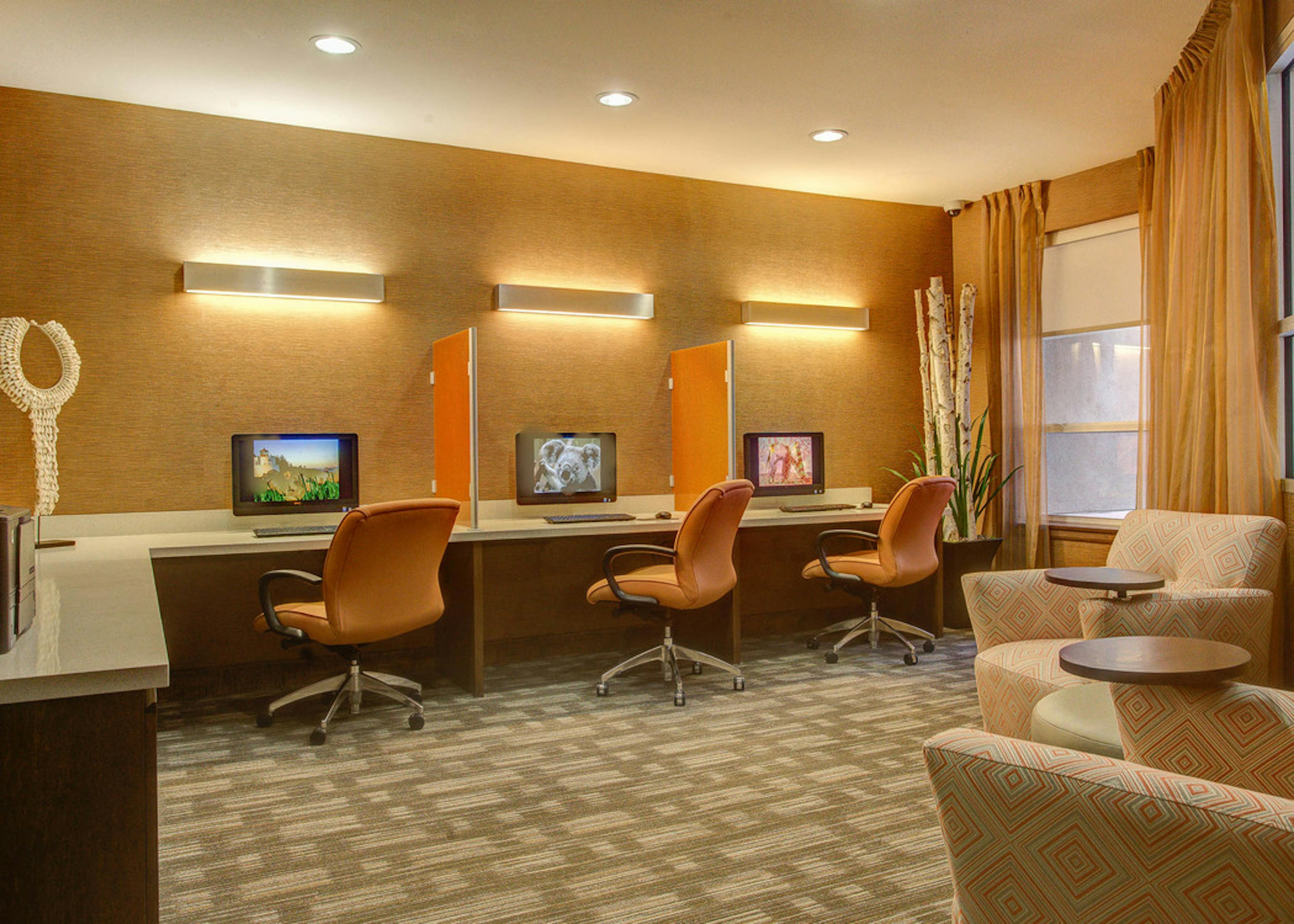 A business center at AMLI Riverfront Park apartments with several computers with rolling chairs as well as other seating area