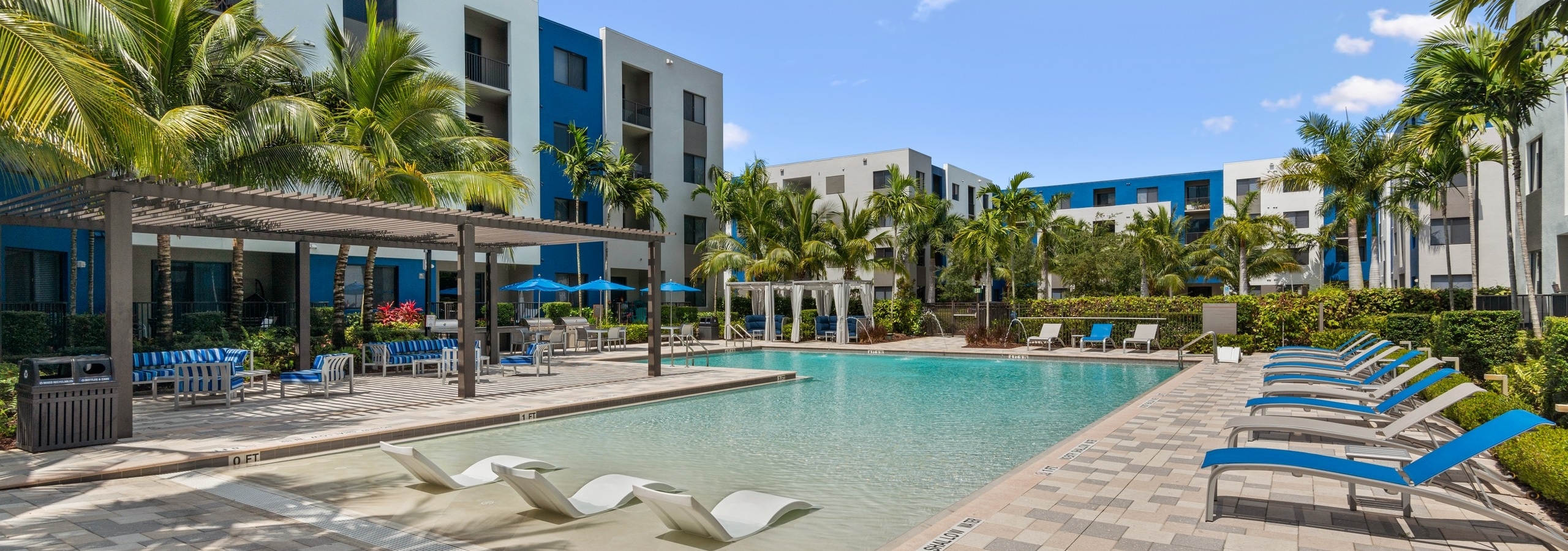 AMLI 8800 pool with white lounge chairs in the water and gray and blue lounge chairs on the pool deck lined with palm trees