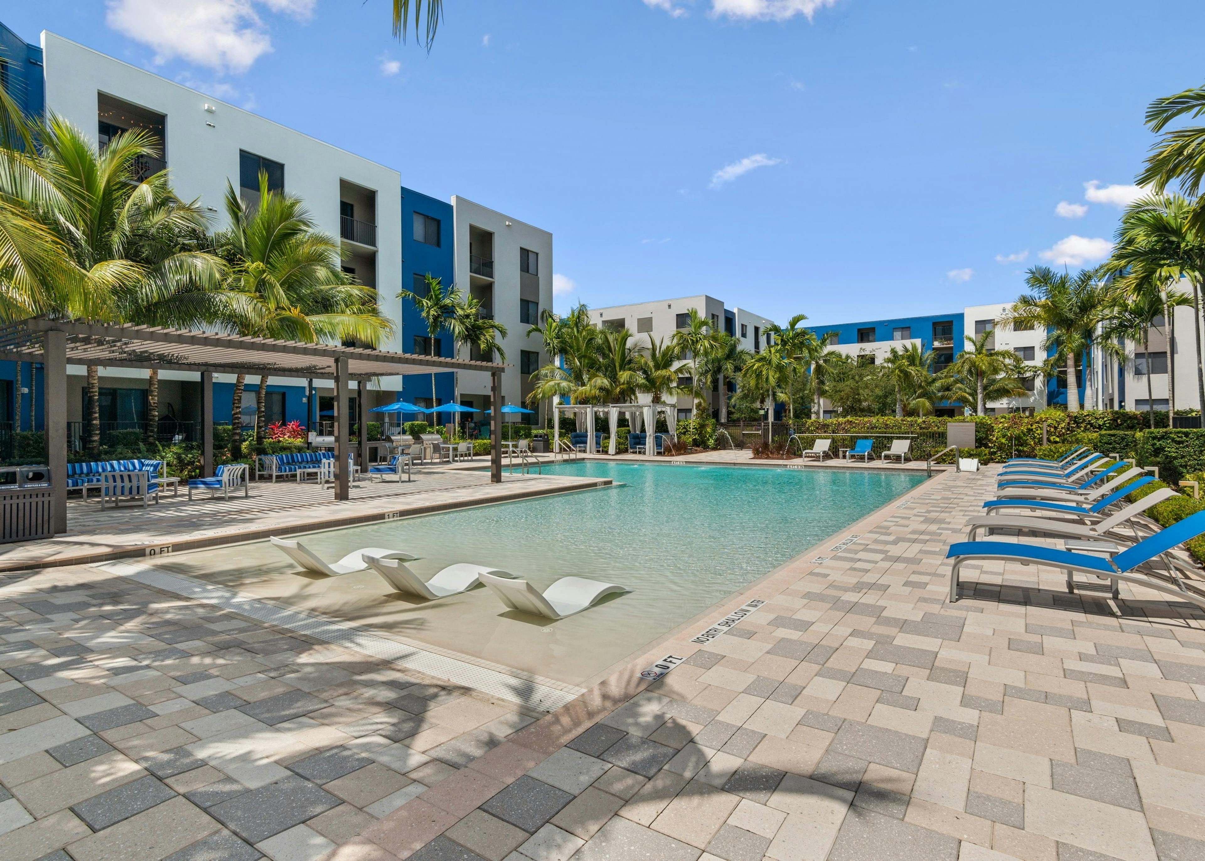 AMLI 8800 pool with white lounge chairs in the water and gray and blue lounge chairs on the pool deck lined with palm trees 