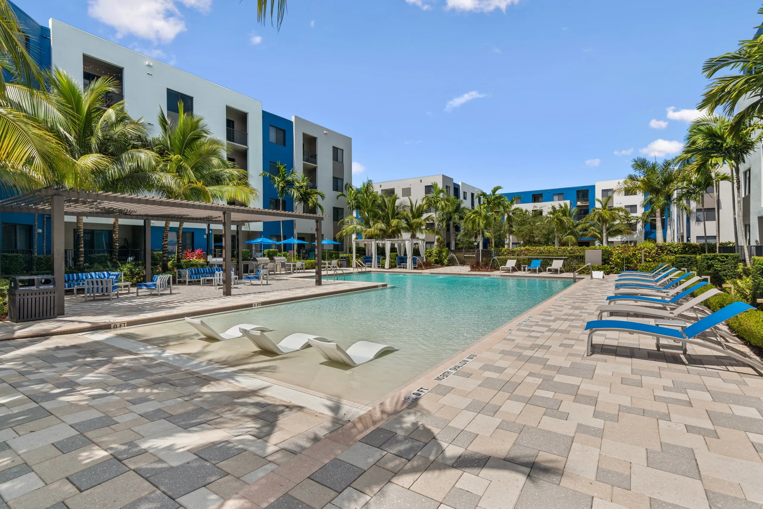 AMLI 8800 pool with white lounge chairs in the water and gray and blue lounge chairs on the pool deck lined with palm trees 