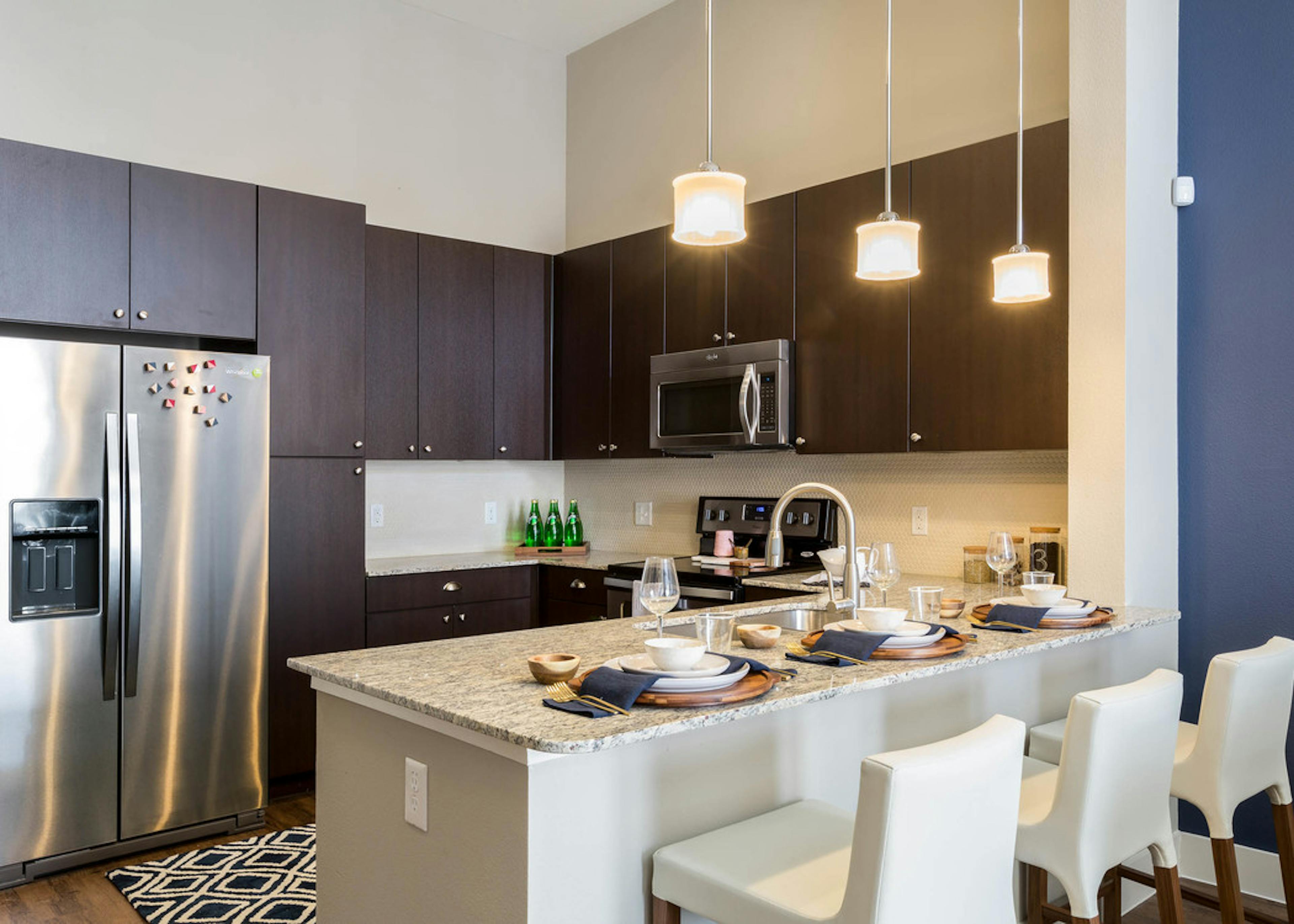 Kitchen at AMLI on Riverside with dark wood cabinets and granite countertops with creme backplash and barstools at counter