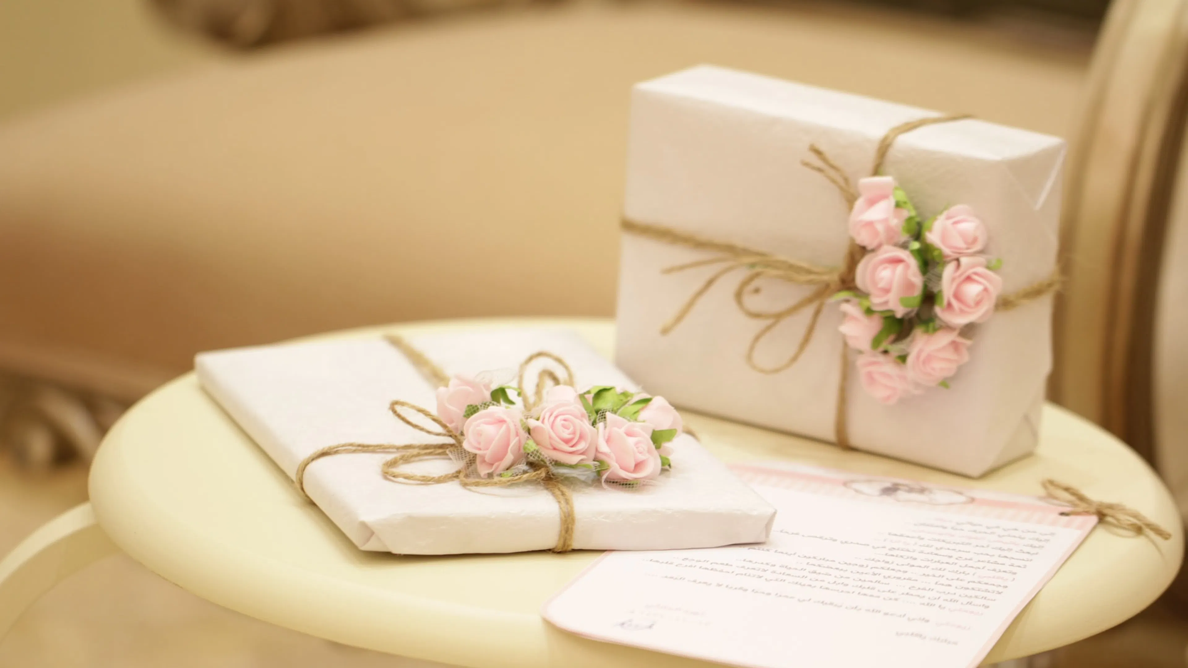 Two white boxes on a table wrapped in white paper tied together with twine and embellished with pink flowers