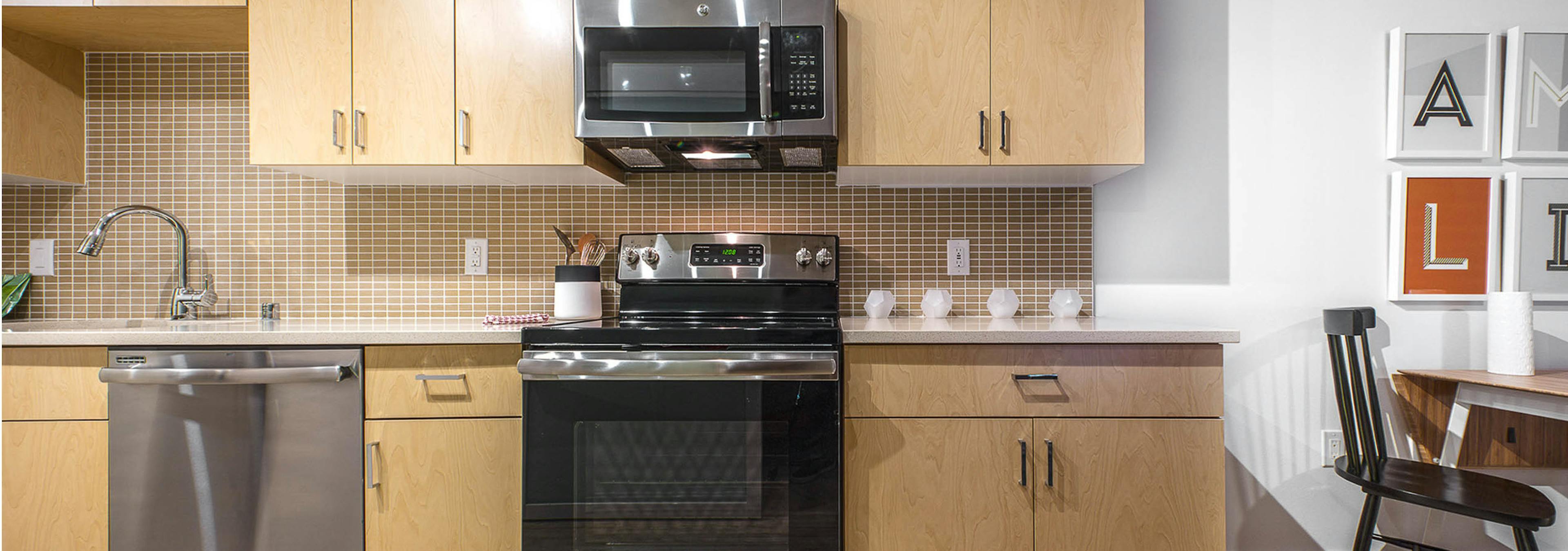 Interior view of an AMLI Wallingford apartment kitchen with light cabinets white quartz counter tops and stainless steel appliances  