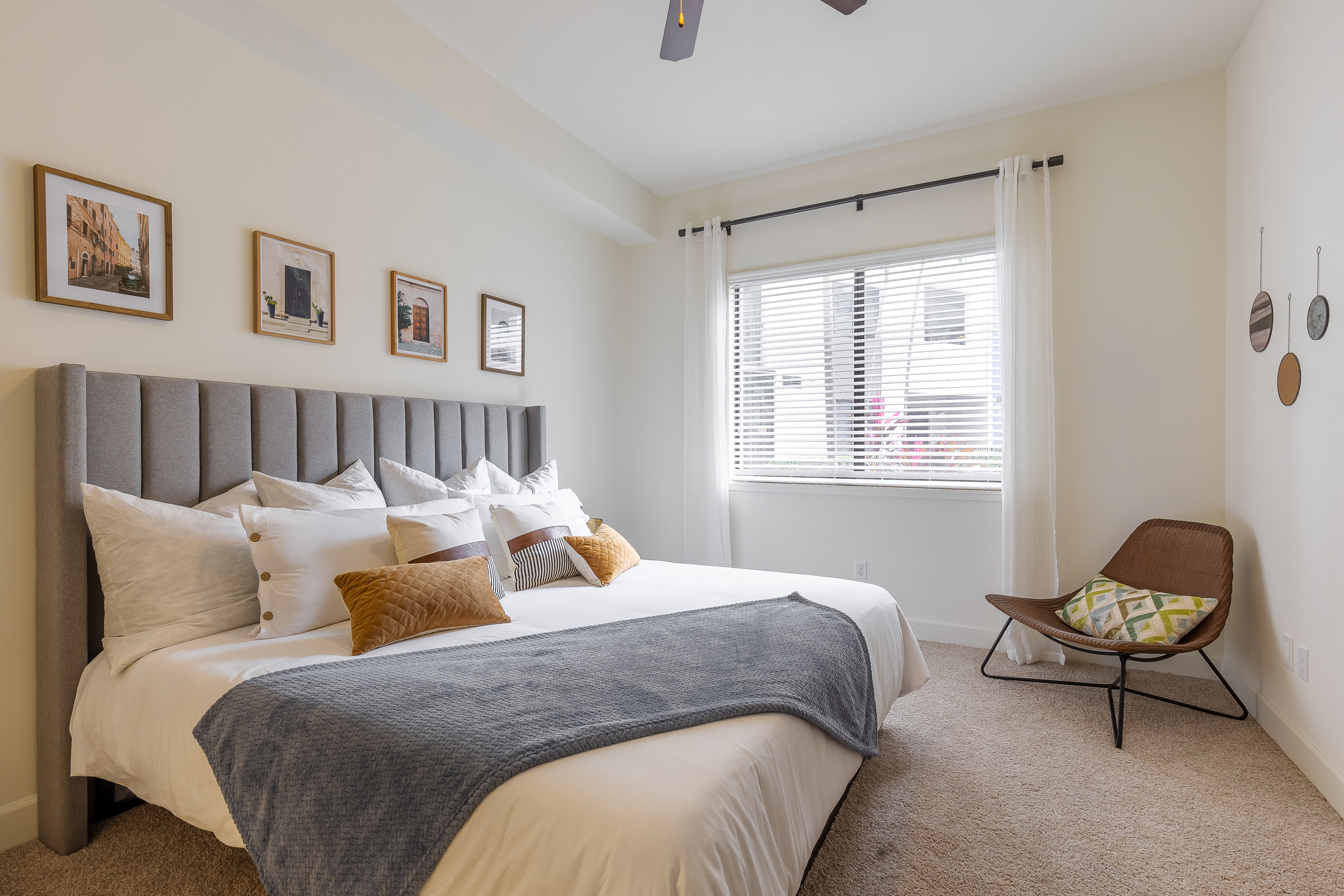 Bedroom at AMLI 8800 with king size bed with multiple pillows against gray headboard and brown chair next to sunny window 