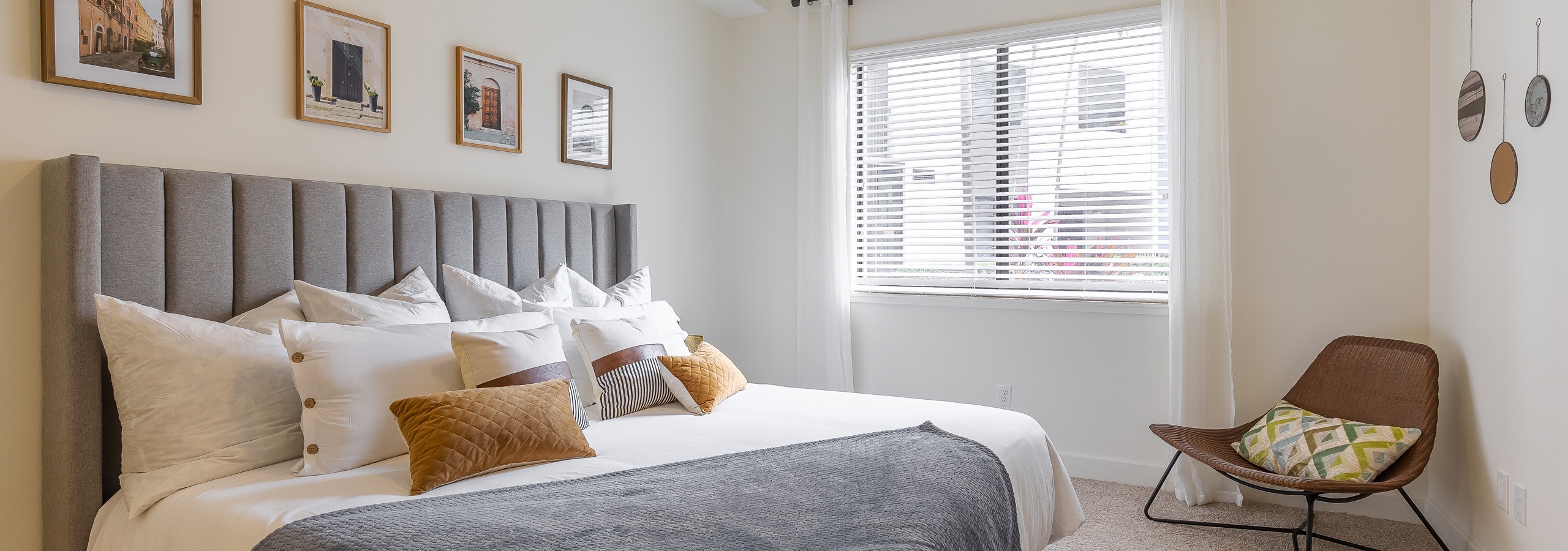 Bedroom at AMLI 8800 with king size bed with multiple pillows against gray headboard and brown chair next to sunny window
