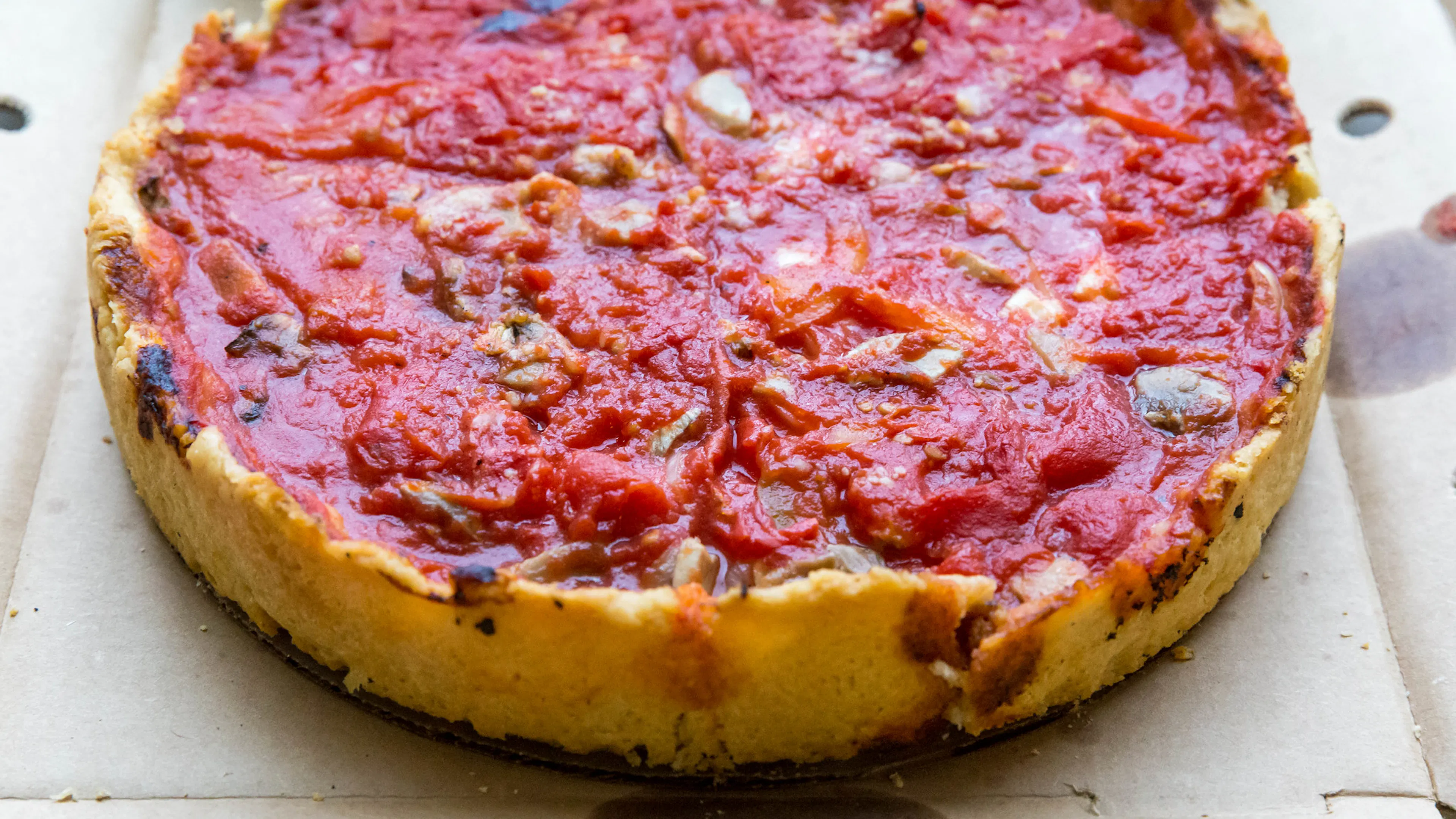 A Chicago style deep dish pizza with thick sauce and vegetable toppings and thin crispy crust in a pizza box