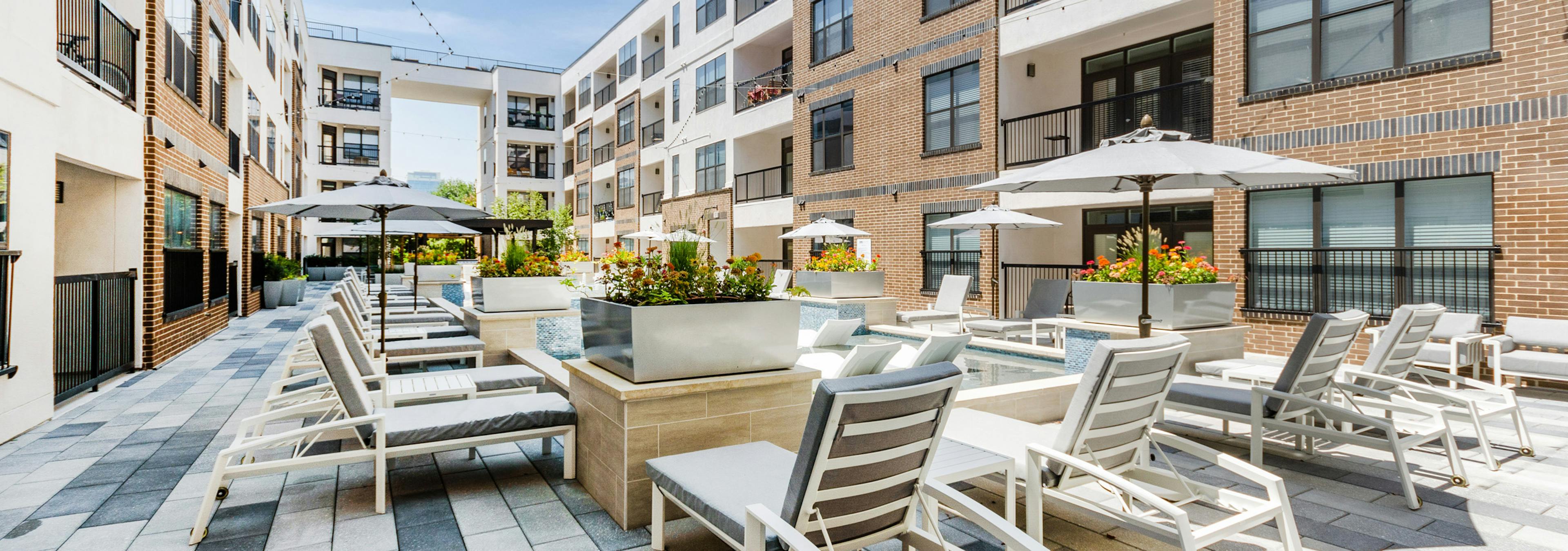 Cooling spa at AMLI Quadrangle apartments with a gray lounge seating shaded by gray umbrellas and flowers in metal planters