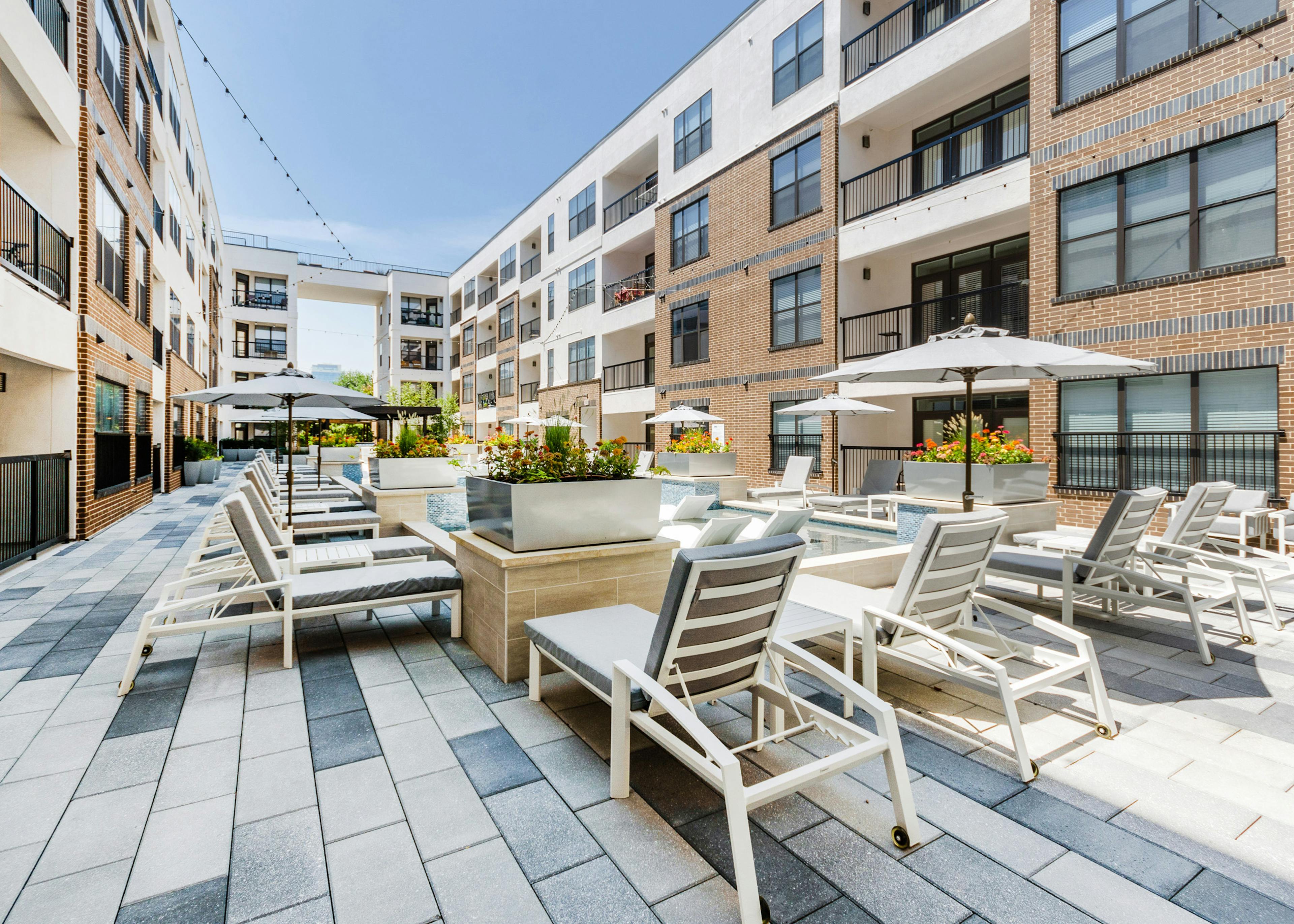 Cooling spa at AMLI Quadrangle apartments with a gray lounge seating shaded by gray umbrellas and flowers in metal planters