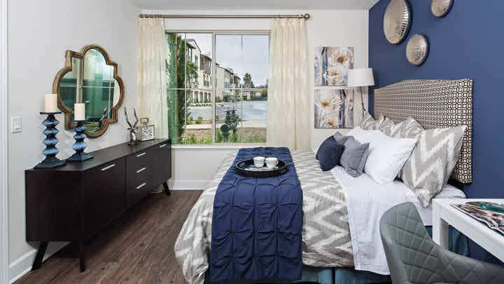 Interior view of AMLI Spanish Hills bedroom with patterned queen upholstered headboard, dresser and window with curtains
