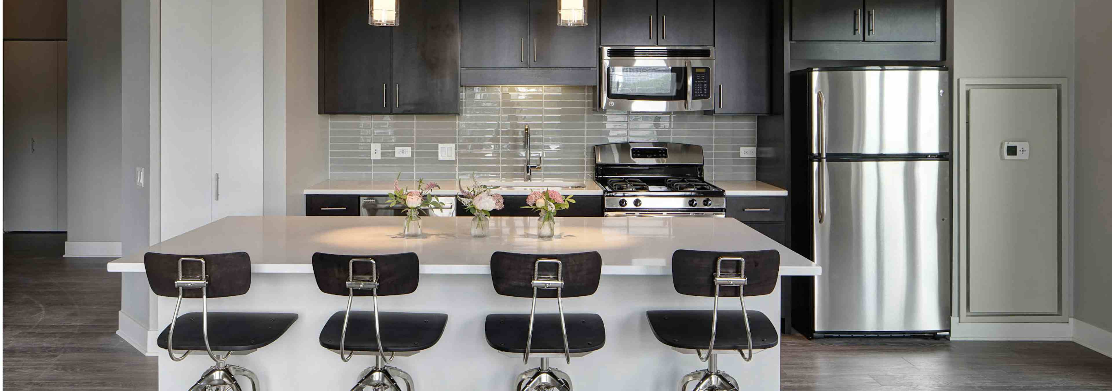 Interior view of an AMLI Lofts kitchen with dark wooden cabinets and a quartz island with four black bar stools