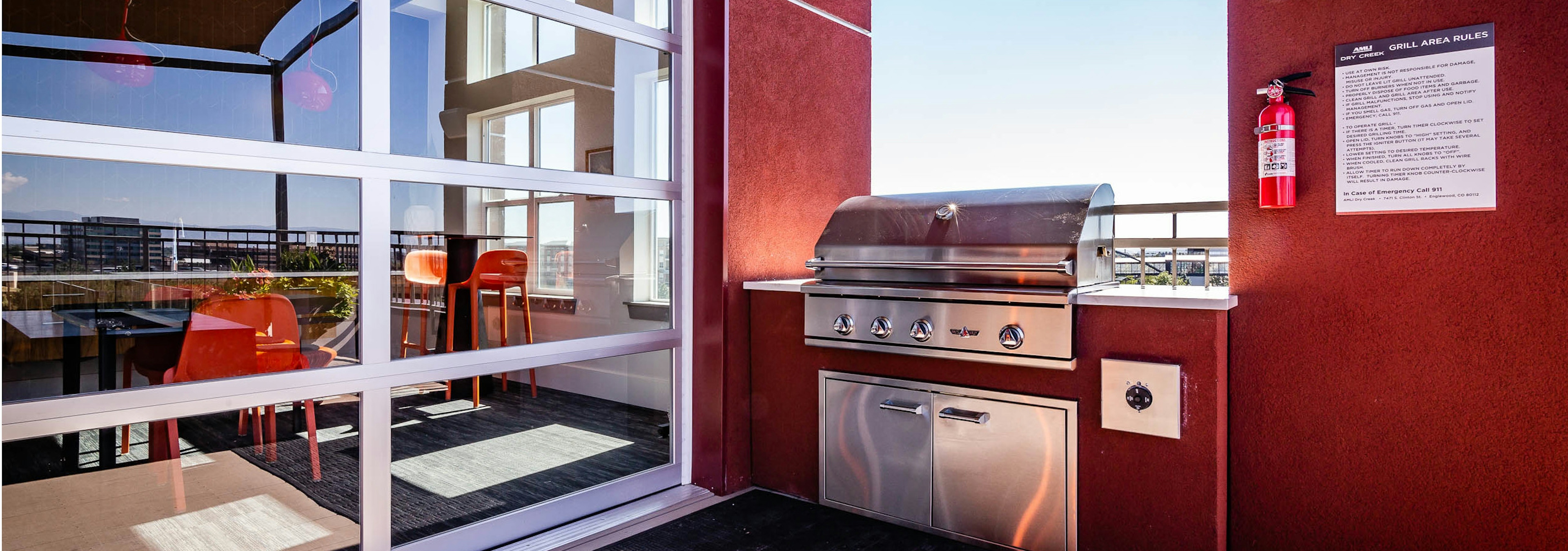 The roof top barbeque area at AMLI Dry Creek apartments with grill and glass garage door with view of lounge with television