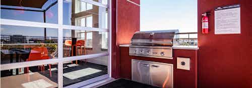 The roof top barbeque area at AMLI Dry Creek apartments with grill and glass garage door with view of lounge with television