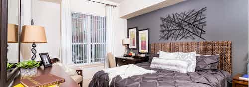 Interior of a bedroom at AMLI Park Avenue apartments with a dark gray bed spread and a wicker head board and a window view