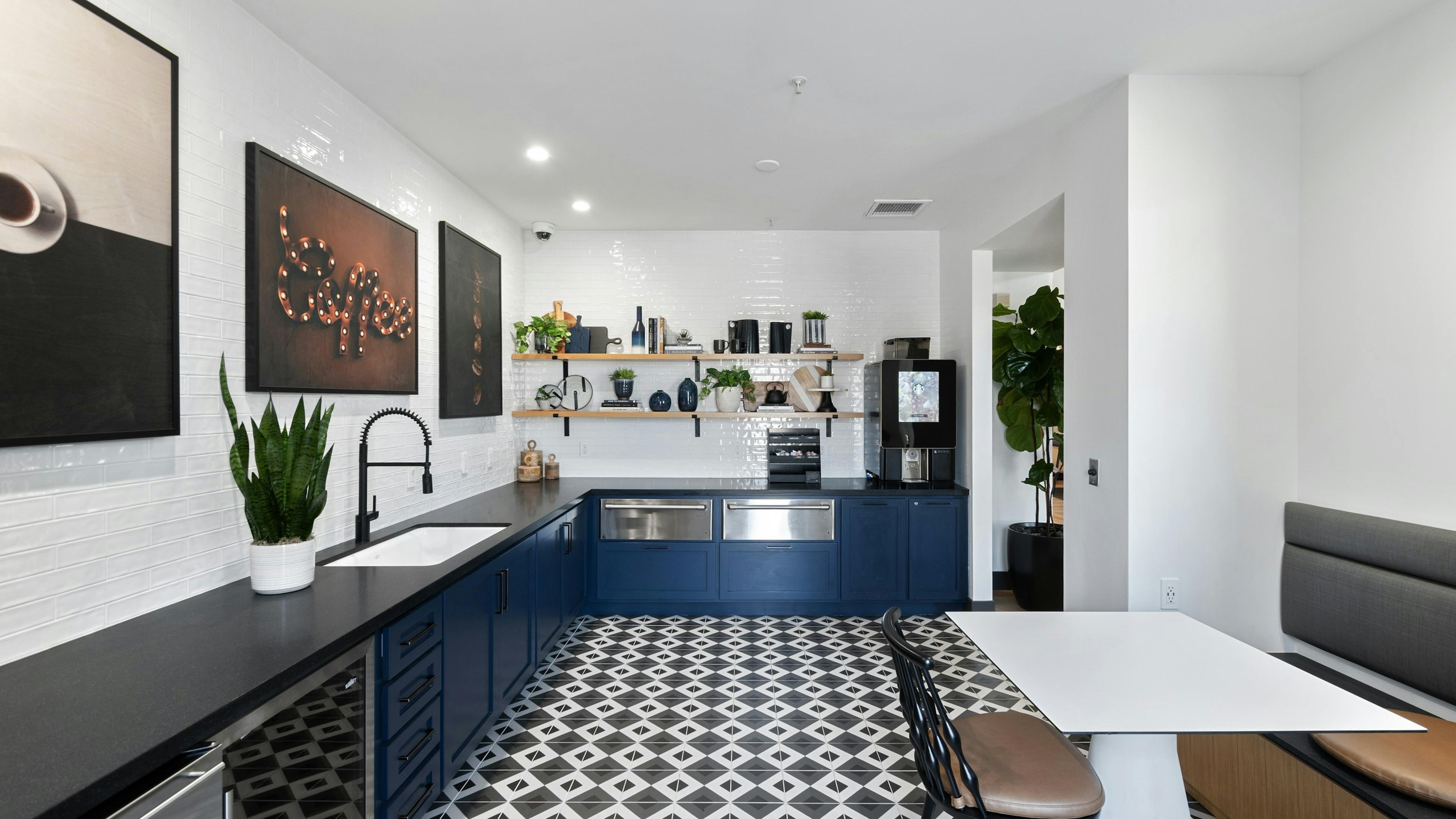 Java bar at AMLI Spanish Hills apartments with blue cabinets and black countertop and pictures shelving on white tile wall