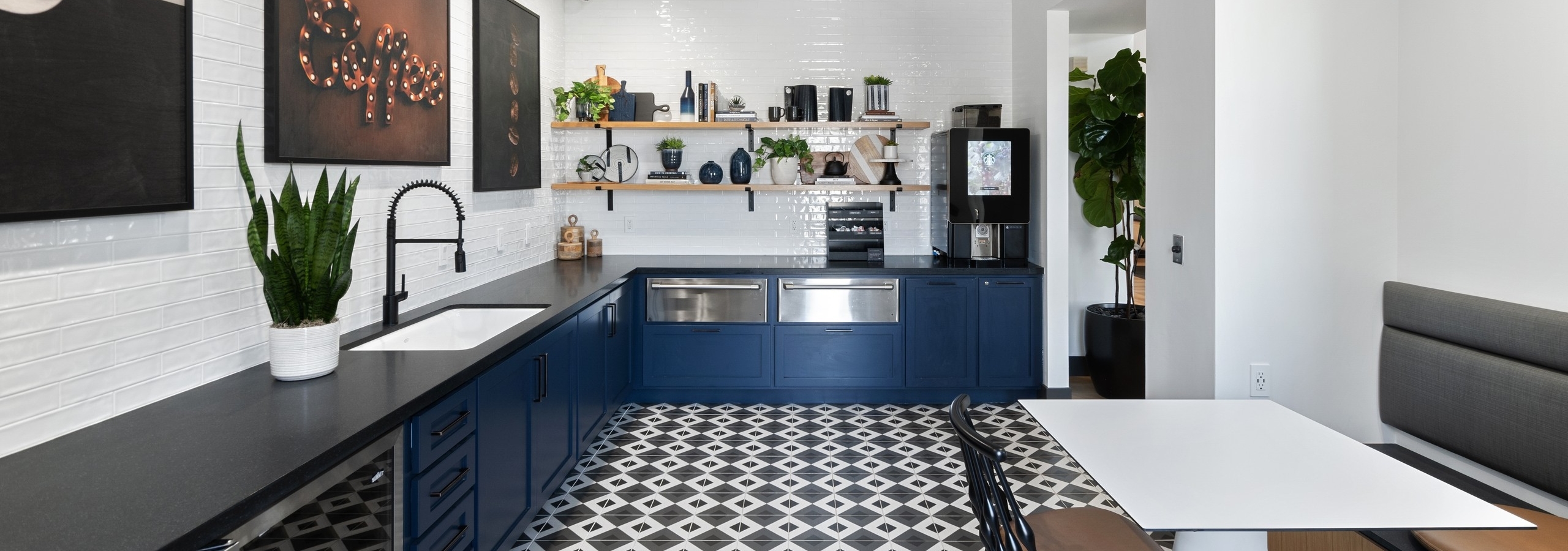 Java bar at AMLI Spanish Hills apartments with blue cabinets and black countertop and pictures shelving on white tile wall