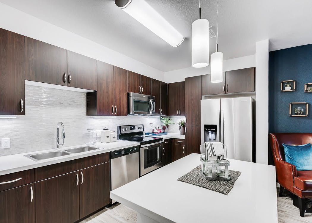 Interior view of a kitchen at AMLI Cherry Creek apartments with an island and white granite counter top and living room chair