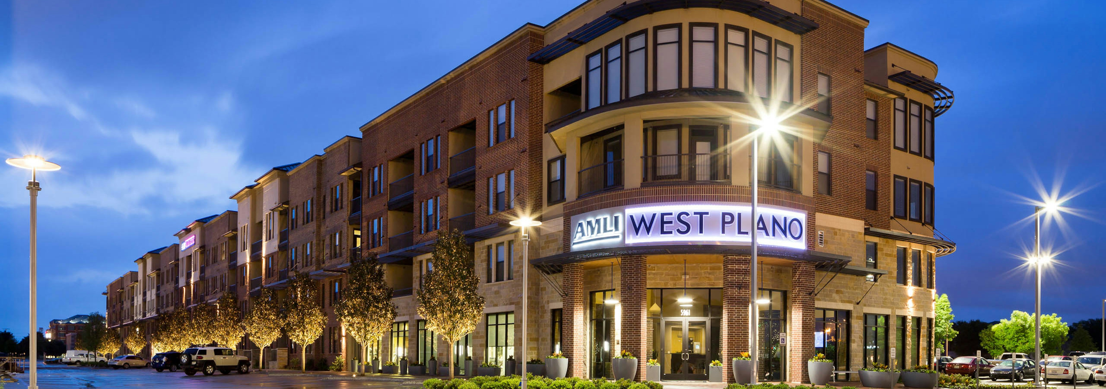 Exterior view of AMLI West Plano at nighttime with brick facade and lamp posts and trees neatly lining the building