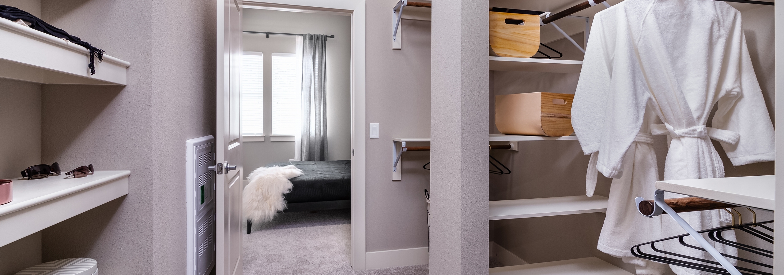 Interior of AMLI Littleton Village apartment’s large closet with shelving, hanging bath robes and peek into master bedroom