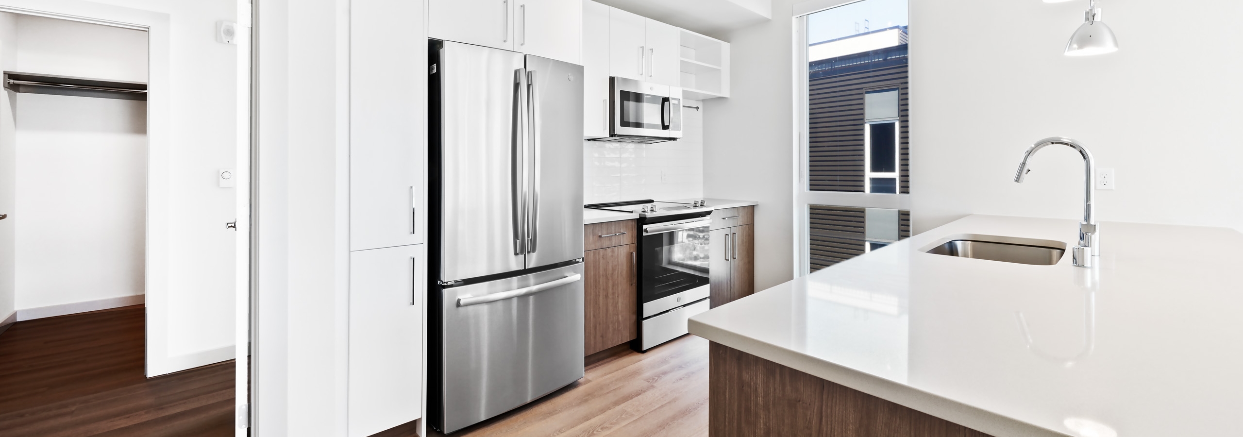 Interior of apartment kitchen at AMLI Spring District with white cabinets and stainless steel appliances and view of bedroom