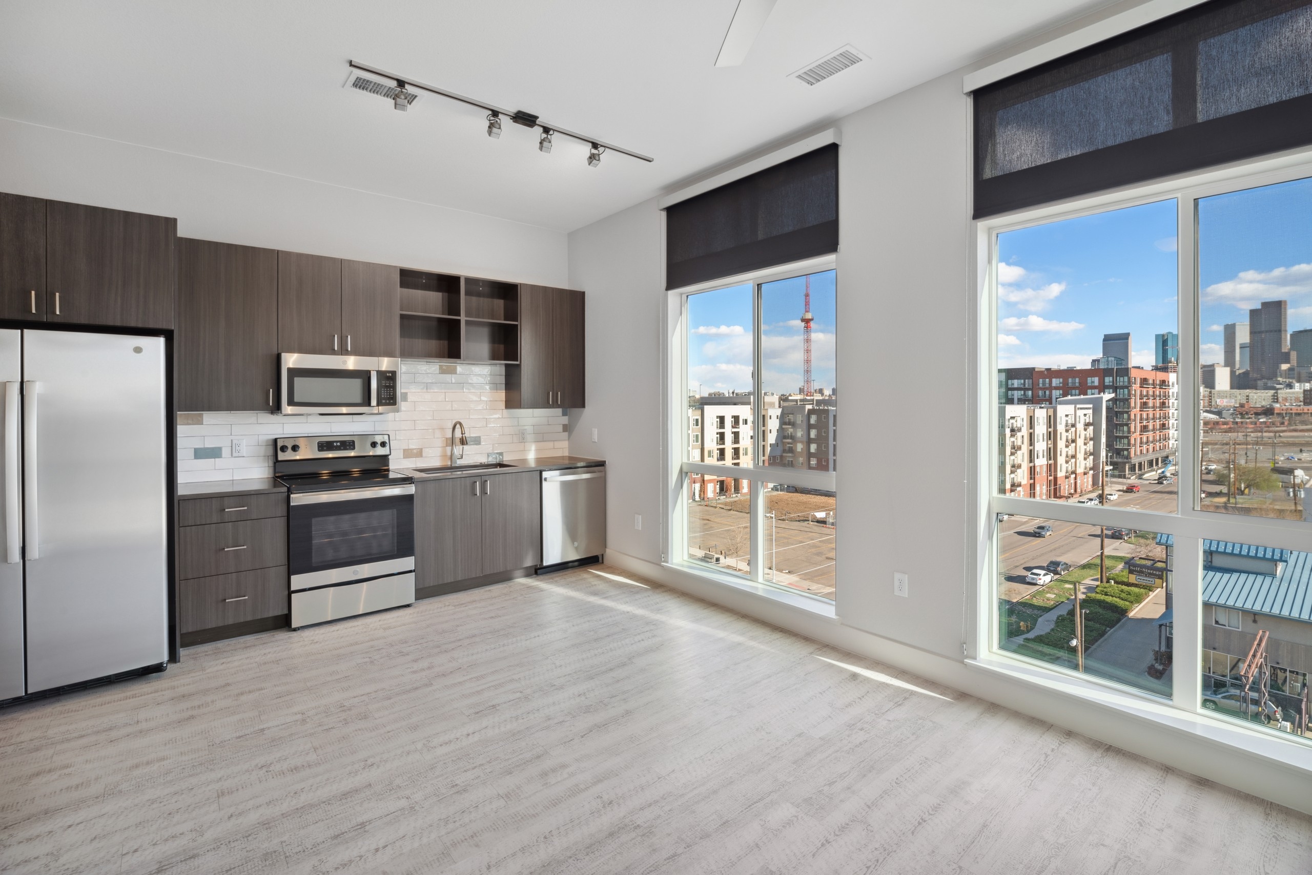 AMLI RiNo kitchen with view of city and brown woodgrain cabinets with stainless steel appliances and white tile backsplash 