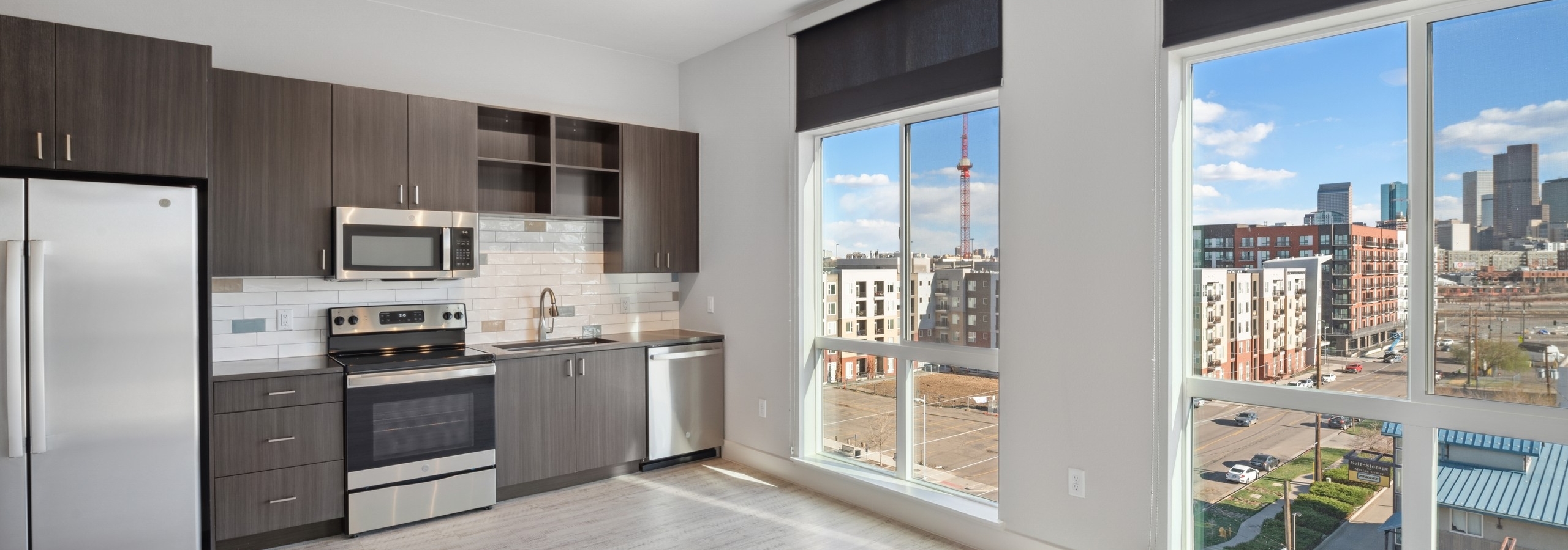 AMLI RiNo kitchen with view of city and brown woodgrain cabinets with stainless steel appliances and white tile backsplash