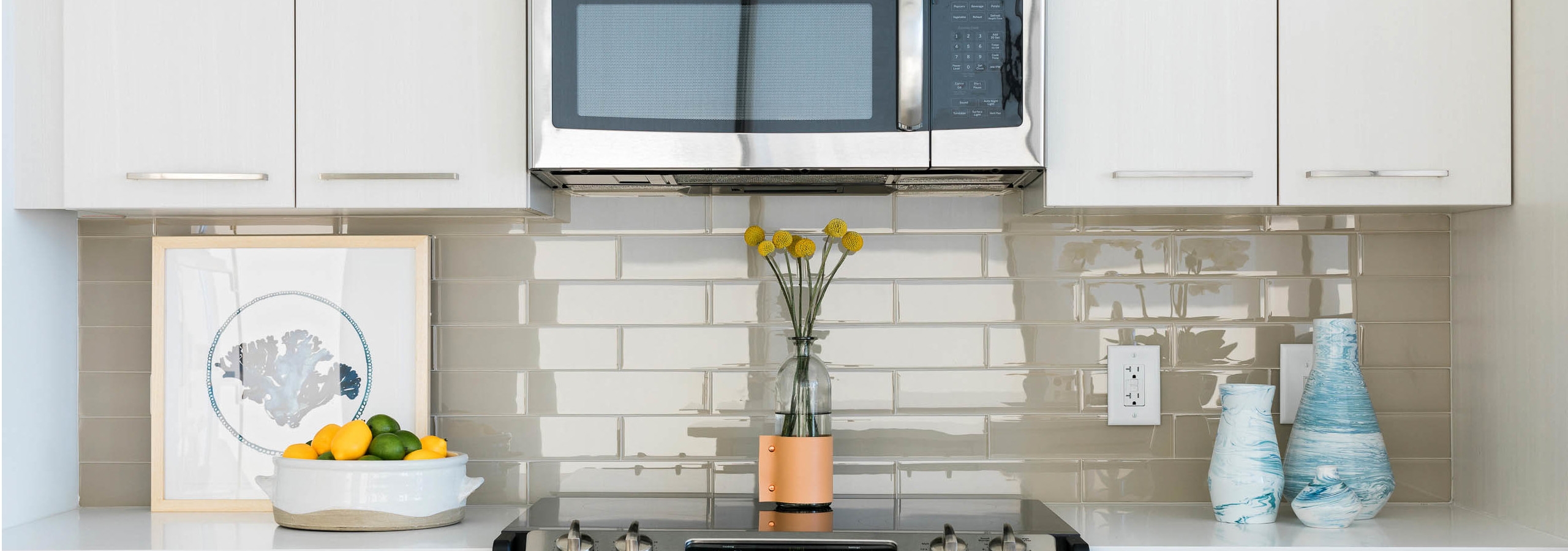 Close up of countertops at AMLI 3464 with a beige tile backplash and a decorative fruit bowl with a vase of yellow flowers