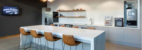 AMLI on 2nd java cafe with grey cabinets and white counters with coffee maker and island with four brown leather barstools