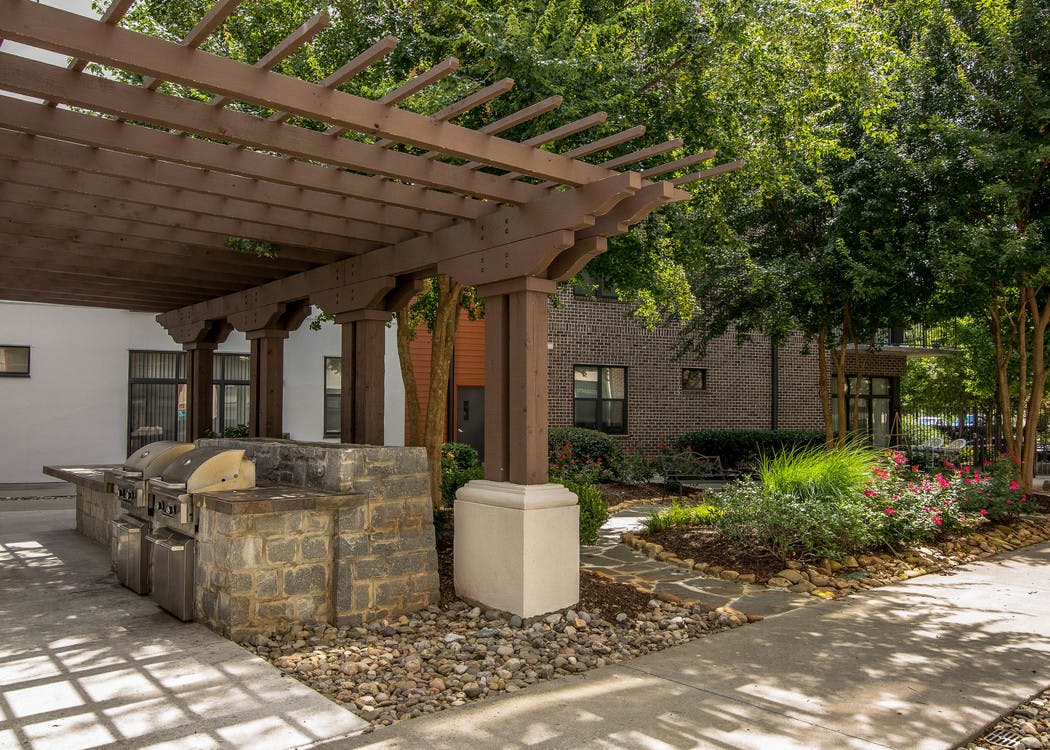 Outdoor grilling area at AMLI Old 4th Ward with stainless steel grills under a shaded trellis next to landscaped trees