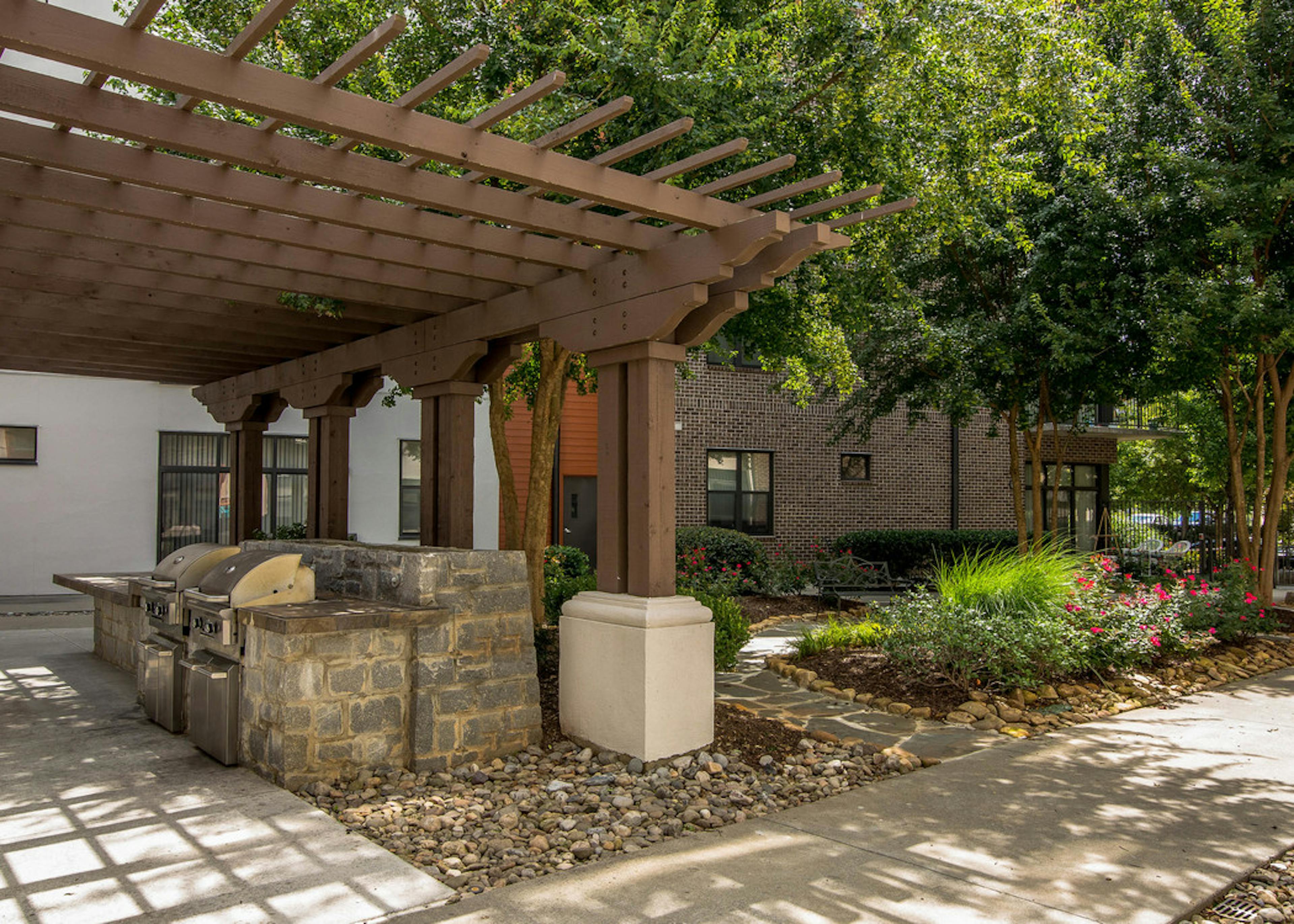 Outdoor grilling area at AMLI Old 4th Ward with stainless steel grills under a shaded trellis next to landscaped trees