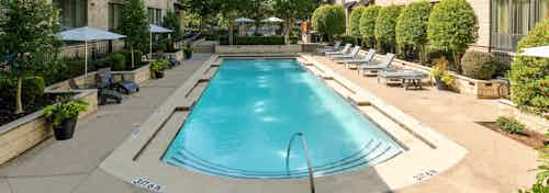 AMLI Las Colinas second pool with surrounding gray lounge chairs and umbrellas and greenery and building on two sides