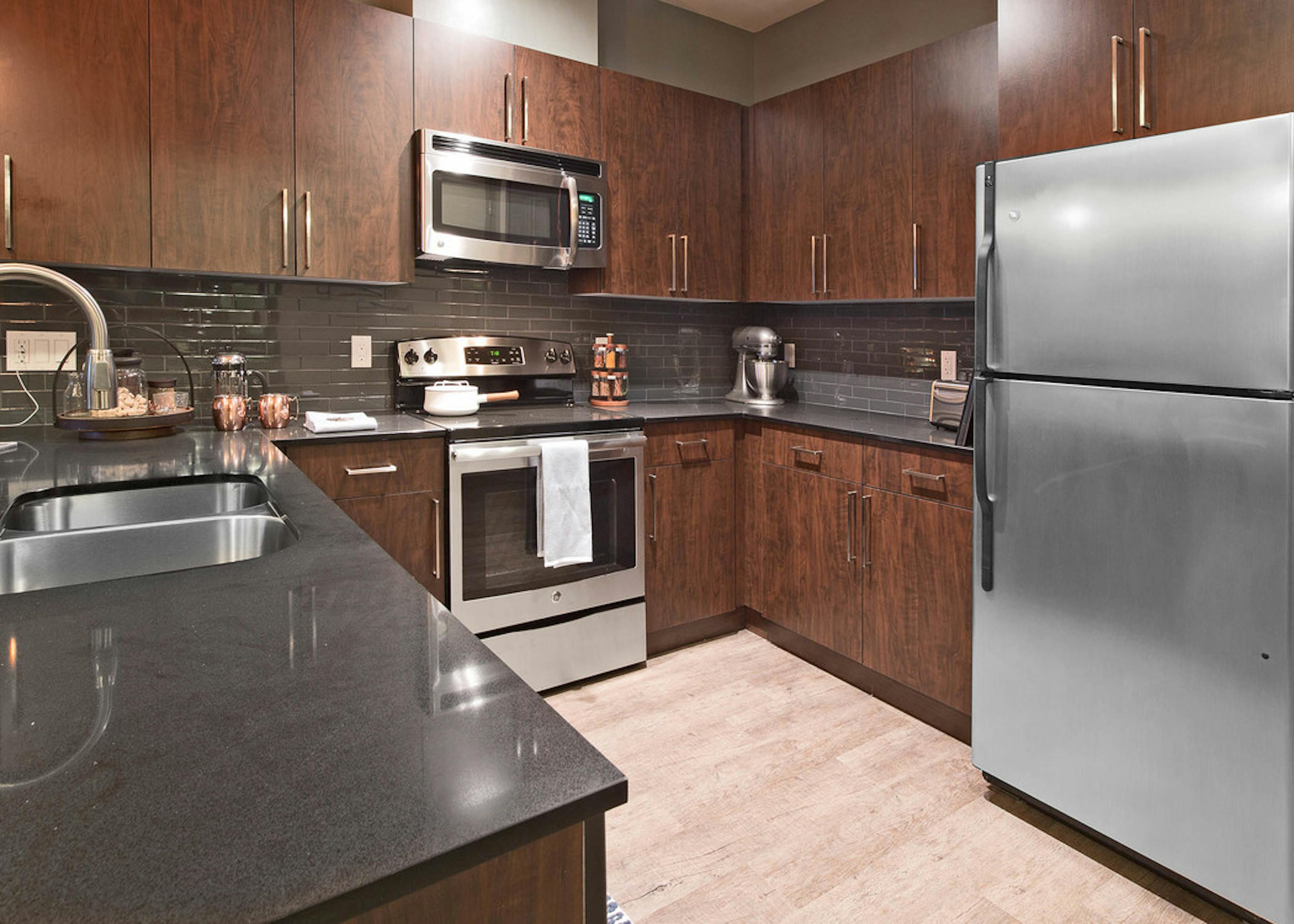 Interior view of AMLI Mark24 apartment kitchen with dark cabinets black back splash black quartz counter tops and stainless steel appliances 